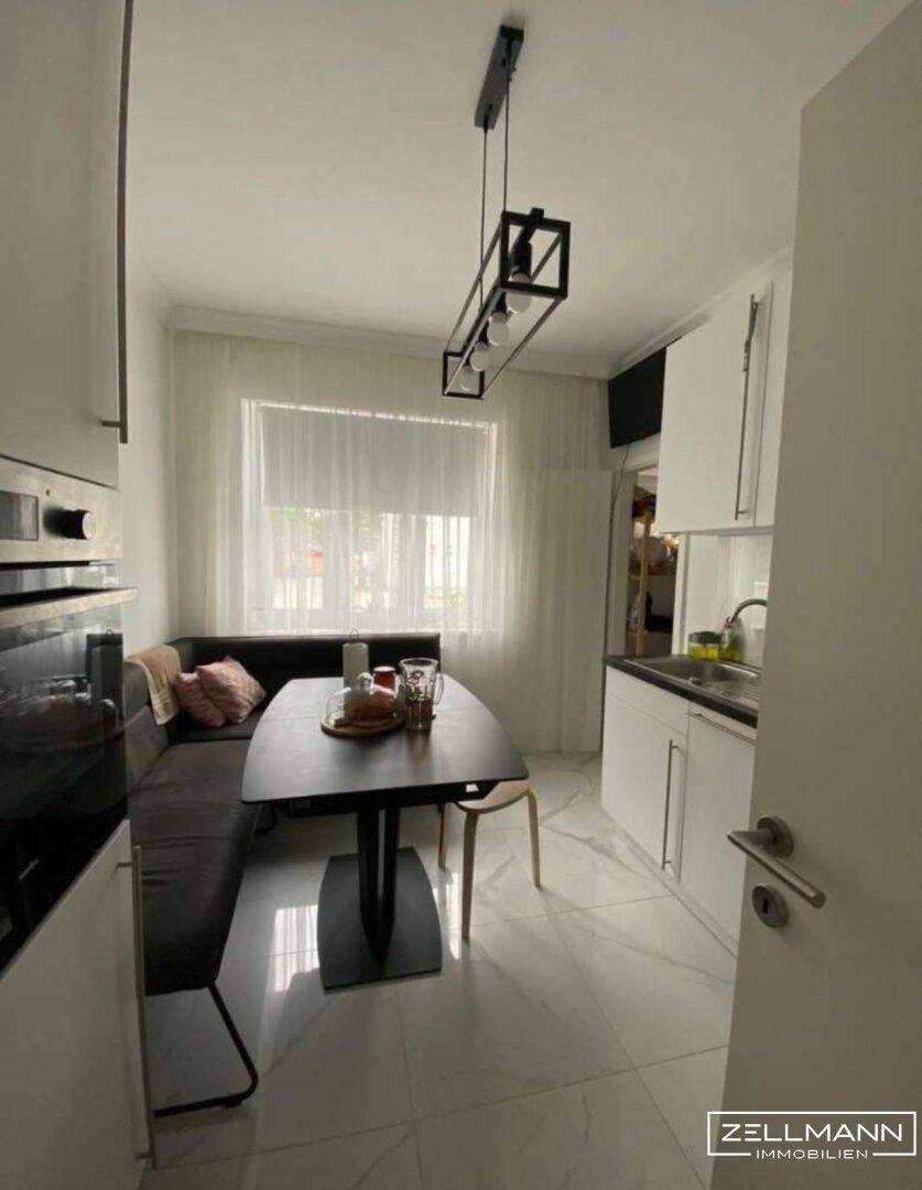 Moderne Küche mit weißen Schränken, Essbereich und Fenster für natürliches Licht.