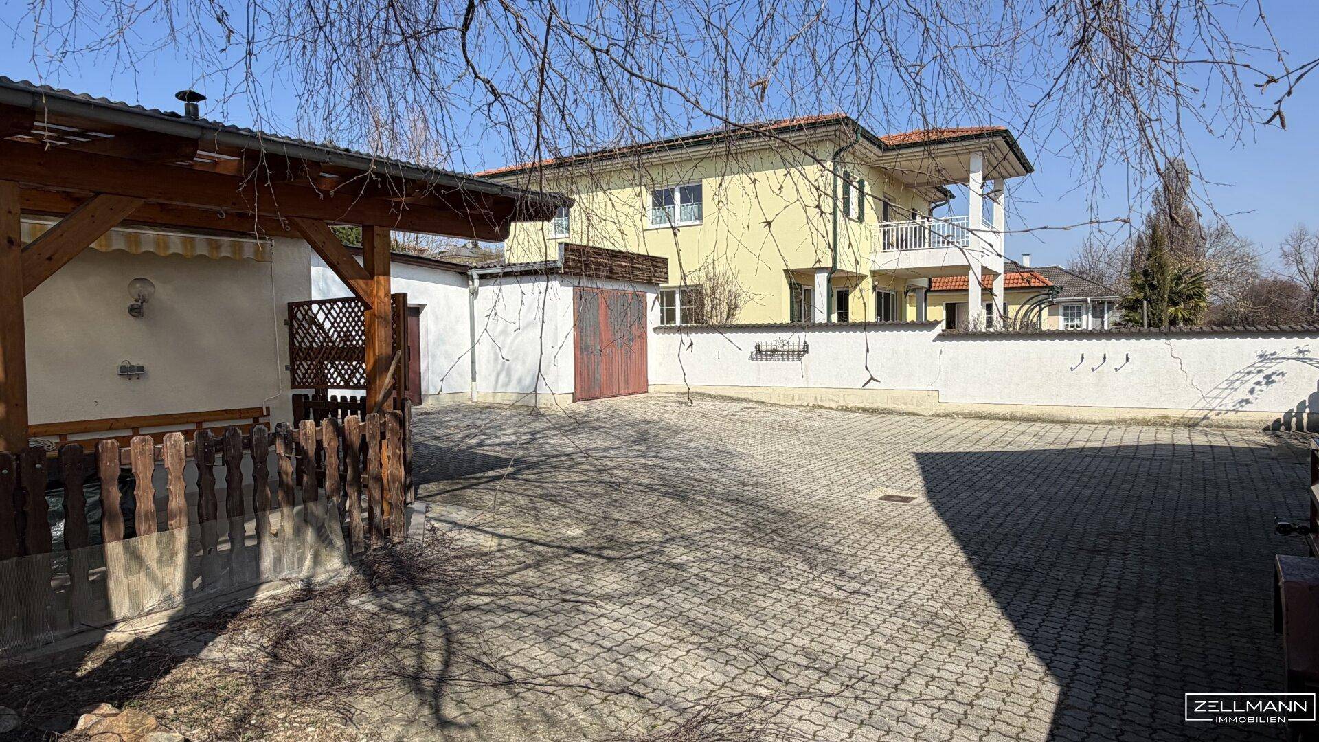Großer gepflasterter Hofbereich mit angrenzendem Gebäude und einer weiteren Villa im Hintergrund.