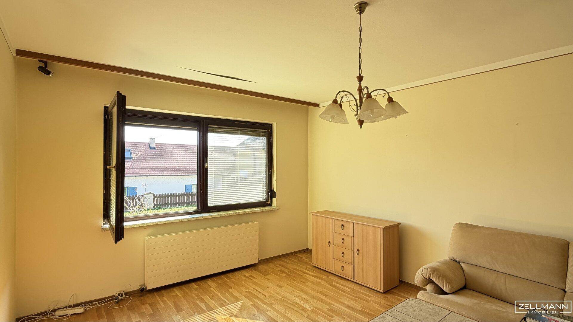 Helles Wohnzimmer mit Parkettboden, großem Fenster und beiger Couch.