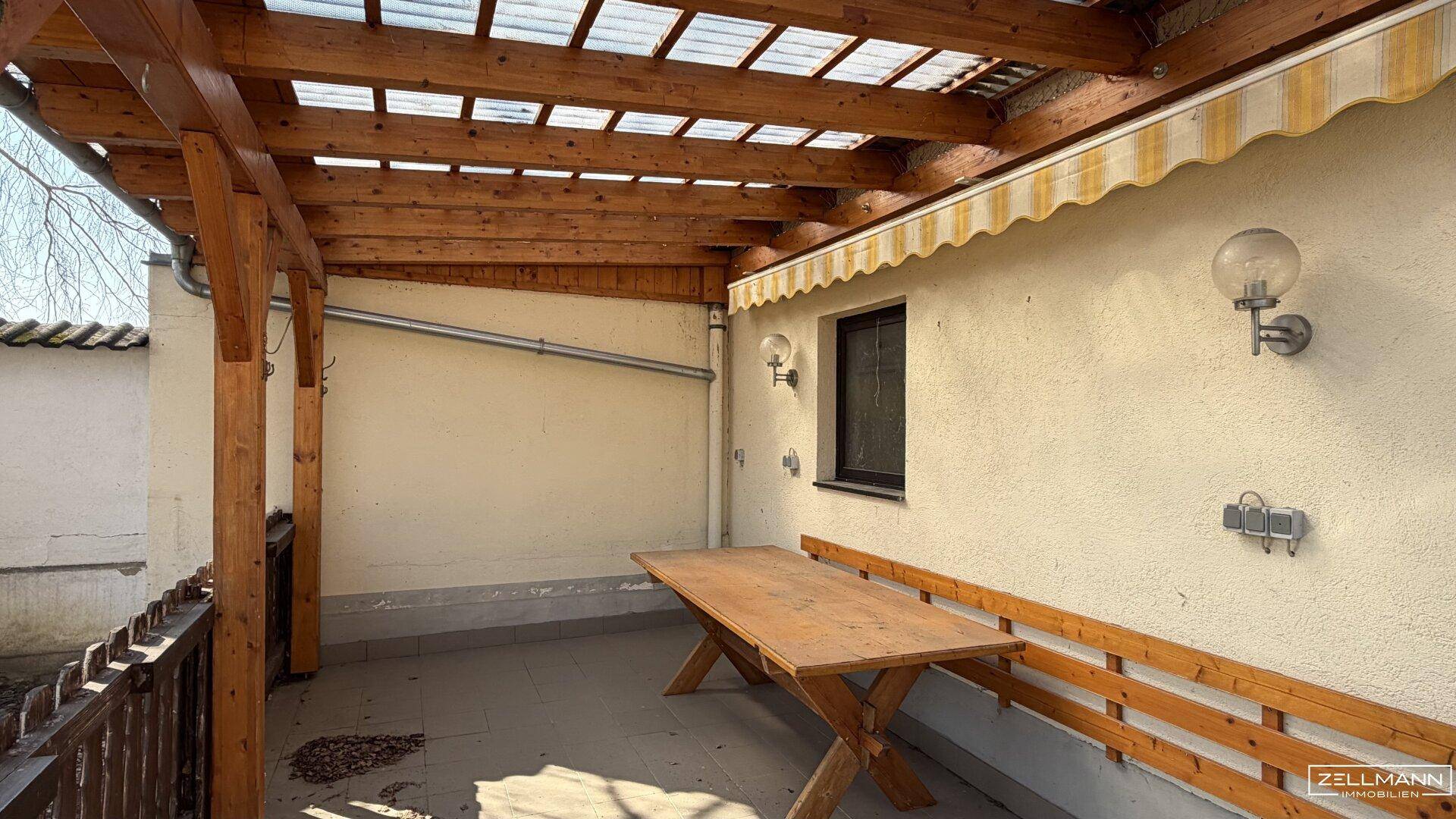 Überdachter Terrassenbereich mit Holzbalken und Sitzgelegenheiten im Freien.