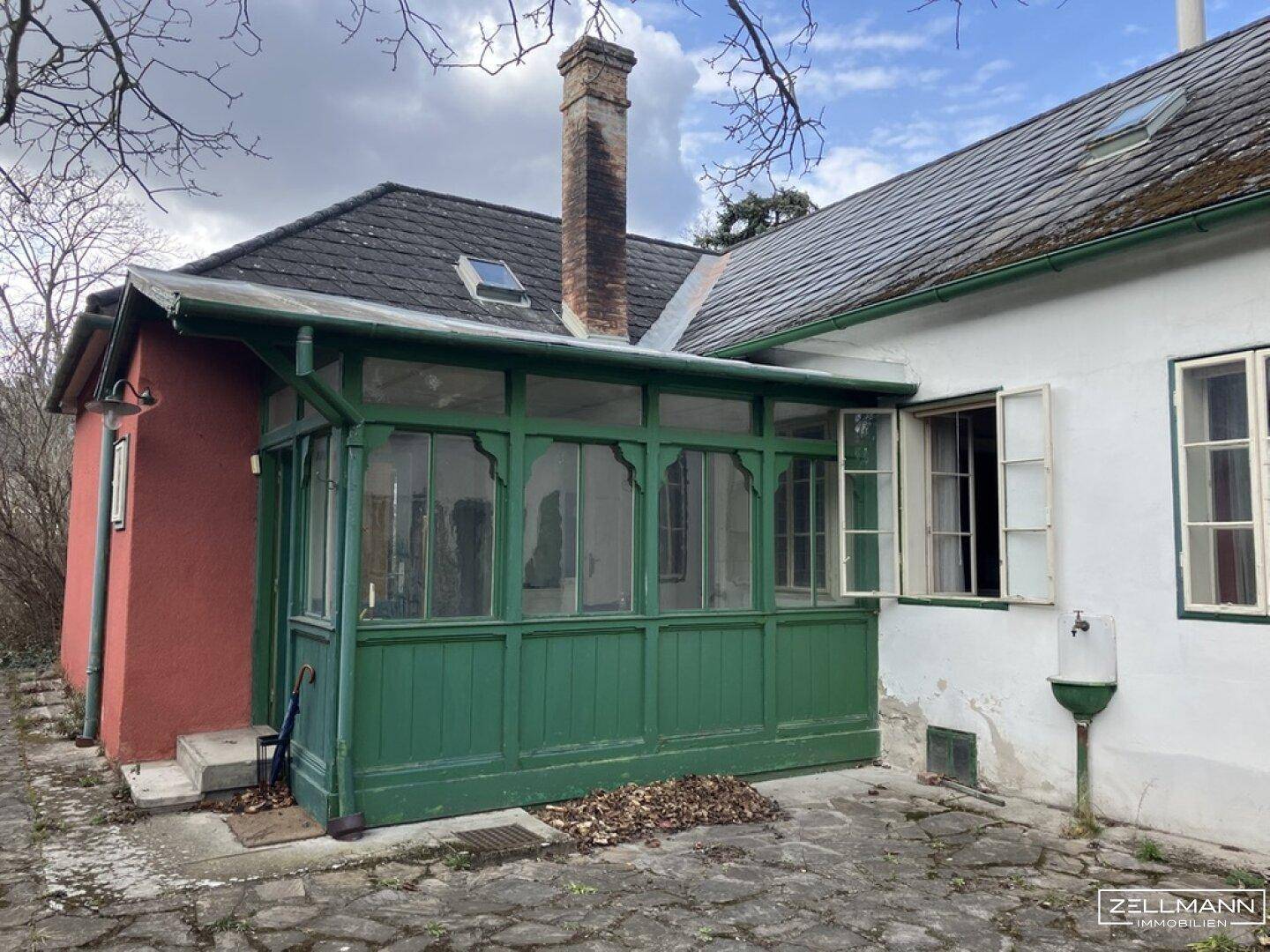Historisches Haus mit einem grünen Wintergarten und einem hohen Ziegelkamin.