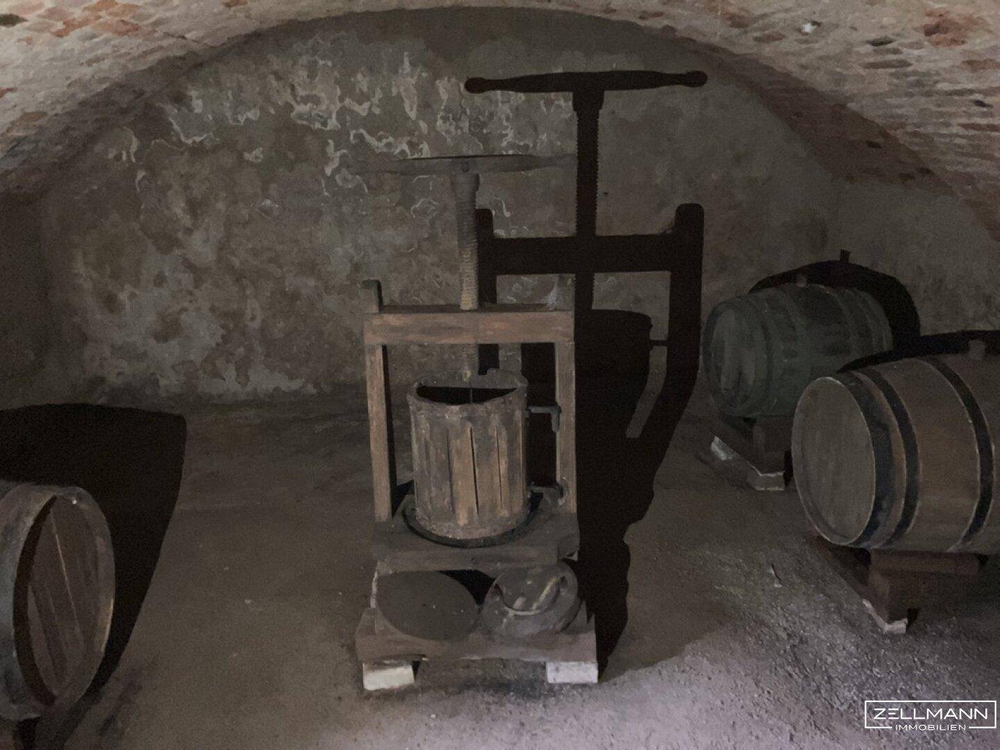 Historischer Gewölbekeller mit Weinfässern und einer alten Weinpresse, ideal für Weinliebhaber.
