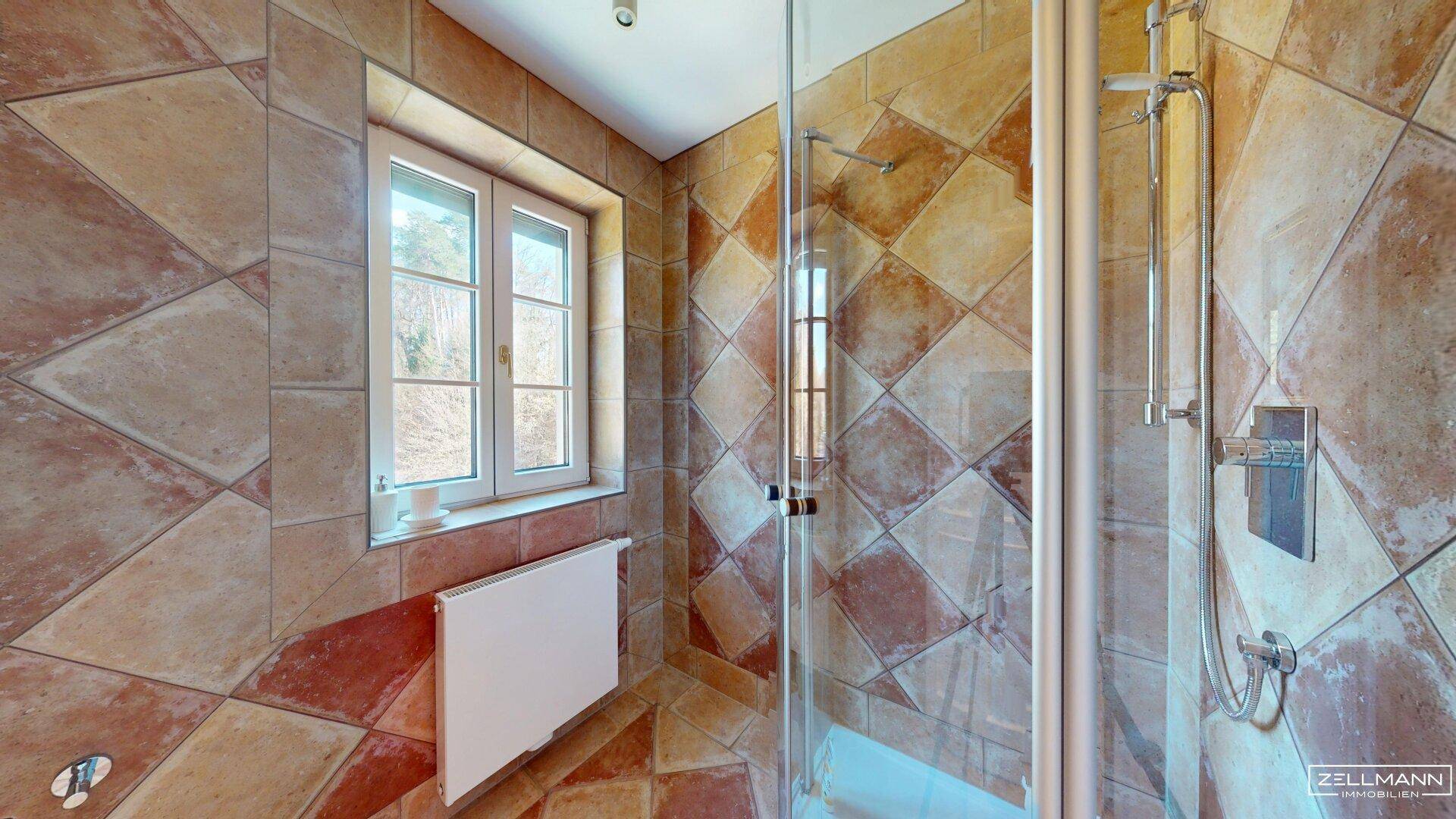 Badezimmer mit gemusterten Terrakotta-Fliesen, Duschkabine und Fenster.