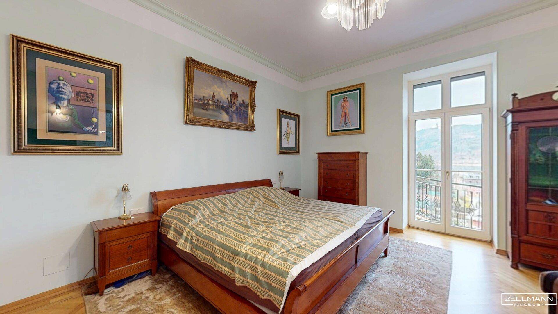 Helles Schlafzimmer mit Parkettboden, klassischem Bett und Zugang zu einem französischen Balkon.