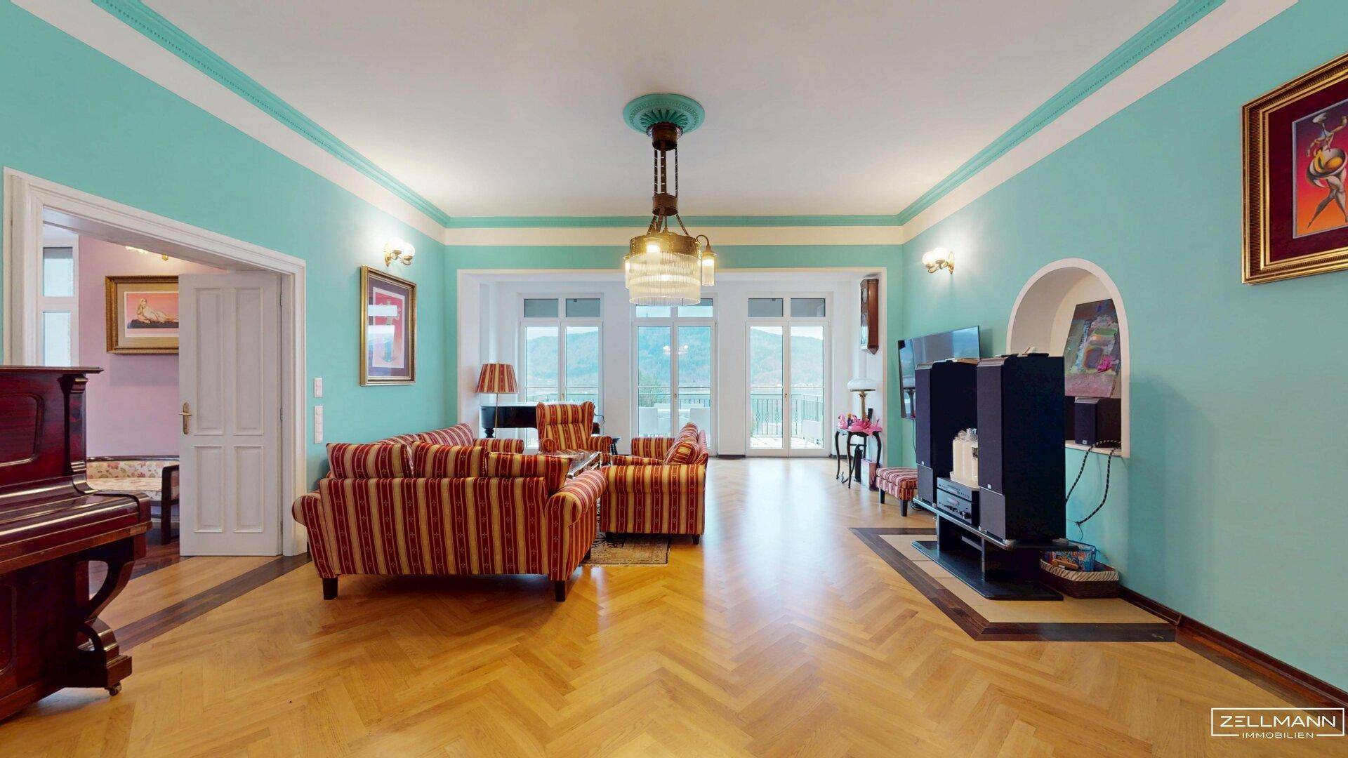 Großzügiges Wohnzimmer mit Fischgrätparkett, farbigen Wänden und Zugang zum Balkon.