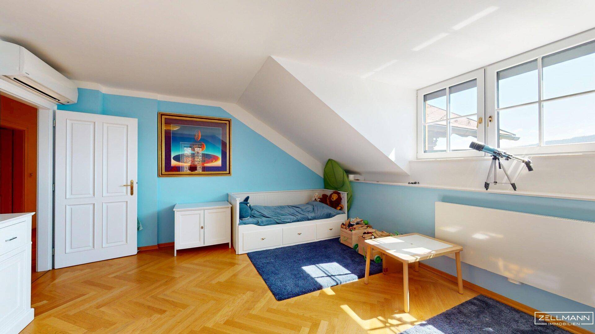 Kinderzimmer im Dachgeschoss mit Schrägen, Parkettboden und blauen Wänden.