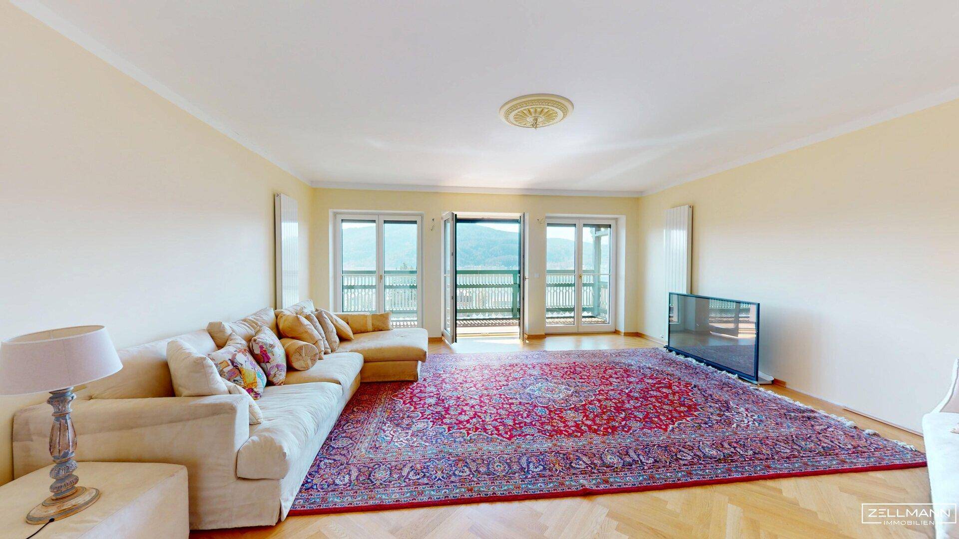 Helles Wohnzimmer mit großem Teppich, beiger Couch und Zugang zu einem Balkon.