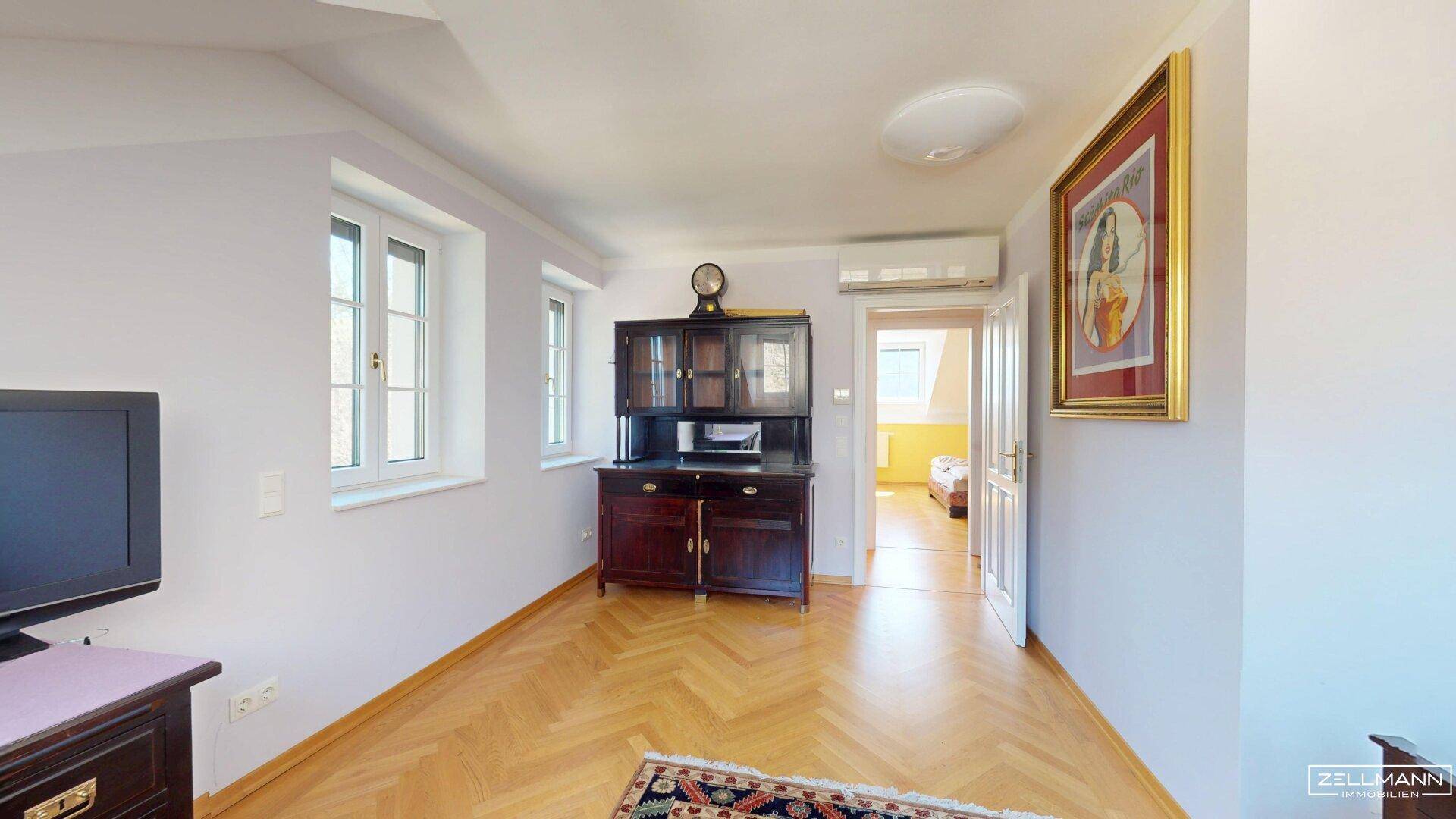 Helles Zimmer mit Parkettboden, Schrank und Blick in den angrenzenden Raum.