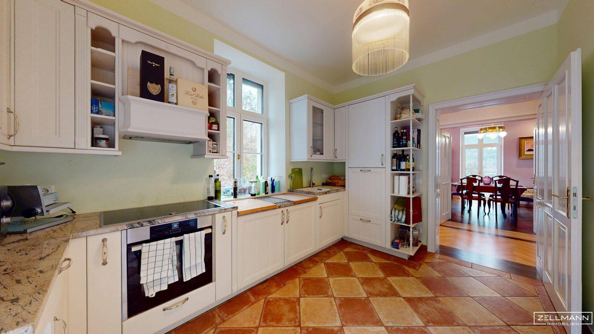 Helle Küche mit Terrakotta-Fliesen, weißen Schränken und Blick ins Esszimmer.
