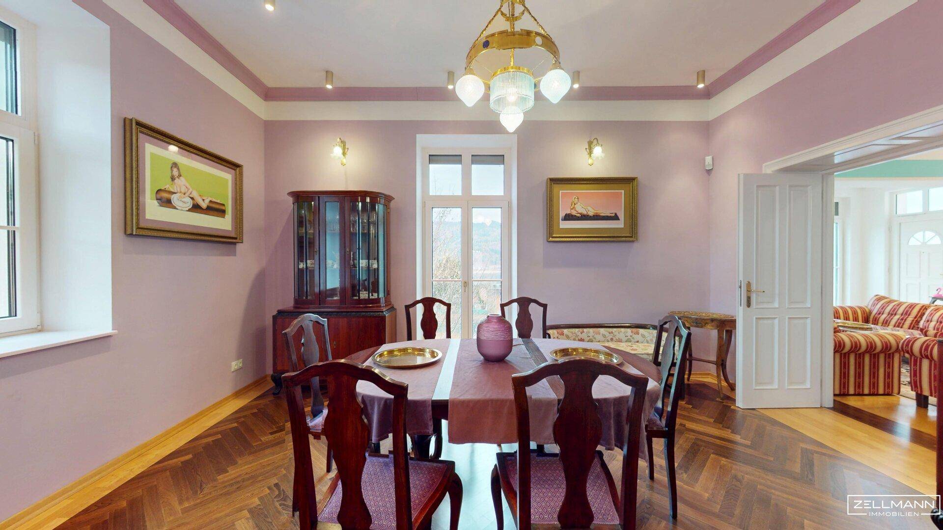Elegantes Esszimmer mit dunklem Fischgrätparkett, lila Wänden und Blick ins Wohnzimmer.