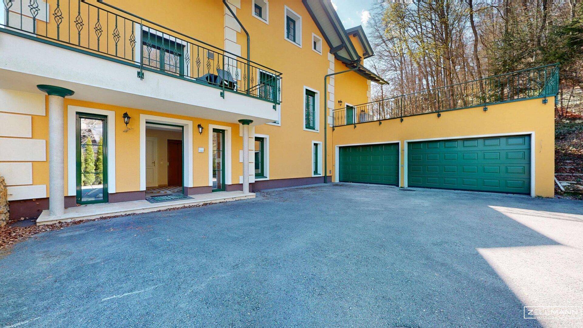 Gelbe Fassade des Hauses mit Balkon, Doppelgarage und großzügiger Auffahrt.