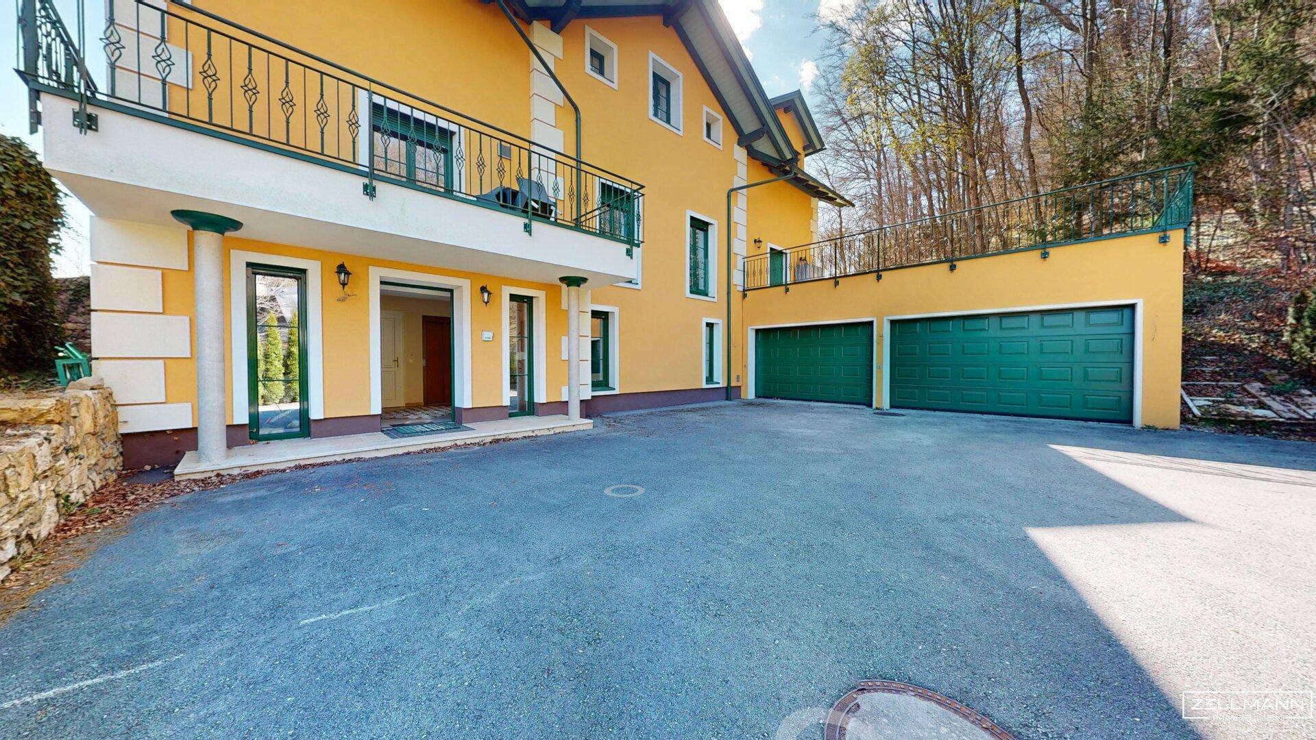 Gelbe Fassade des Hauses mit Balkon, Doppelgarage und großzügiger Auffahrt.
