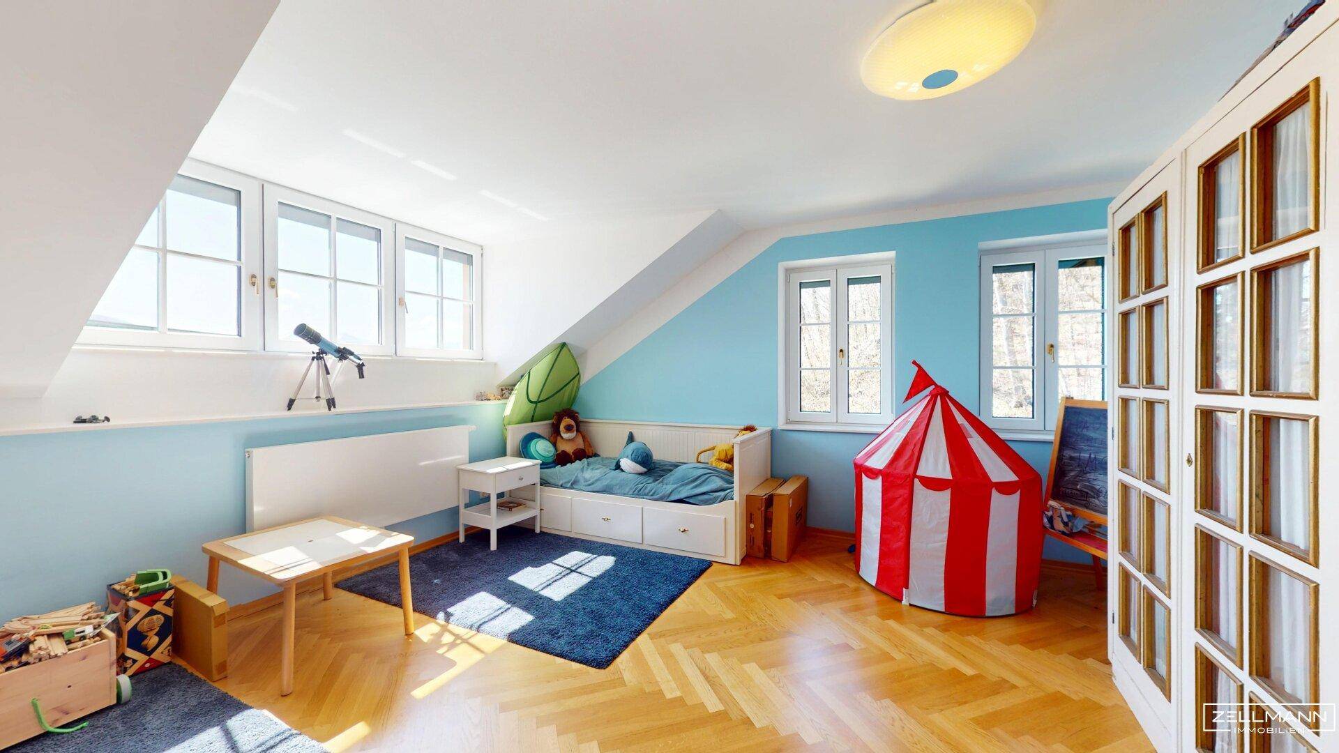 Kinderzimmer im Dachgeschoss mit Schrägen, Parkettboden und blauen Wänden.