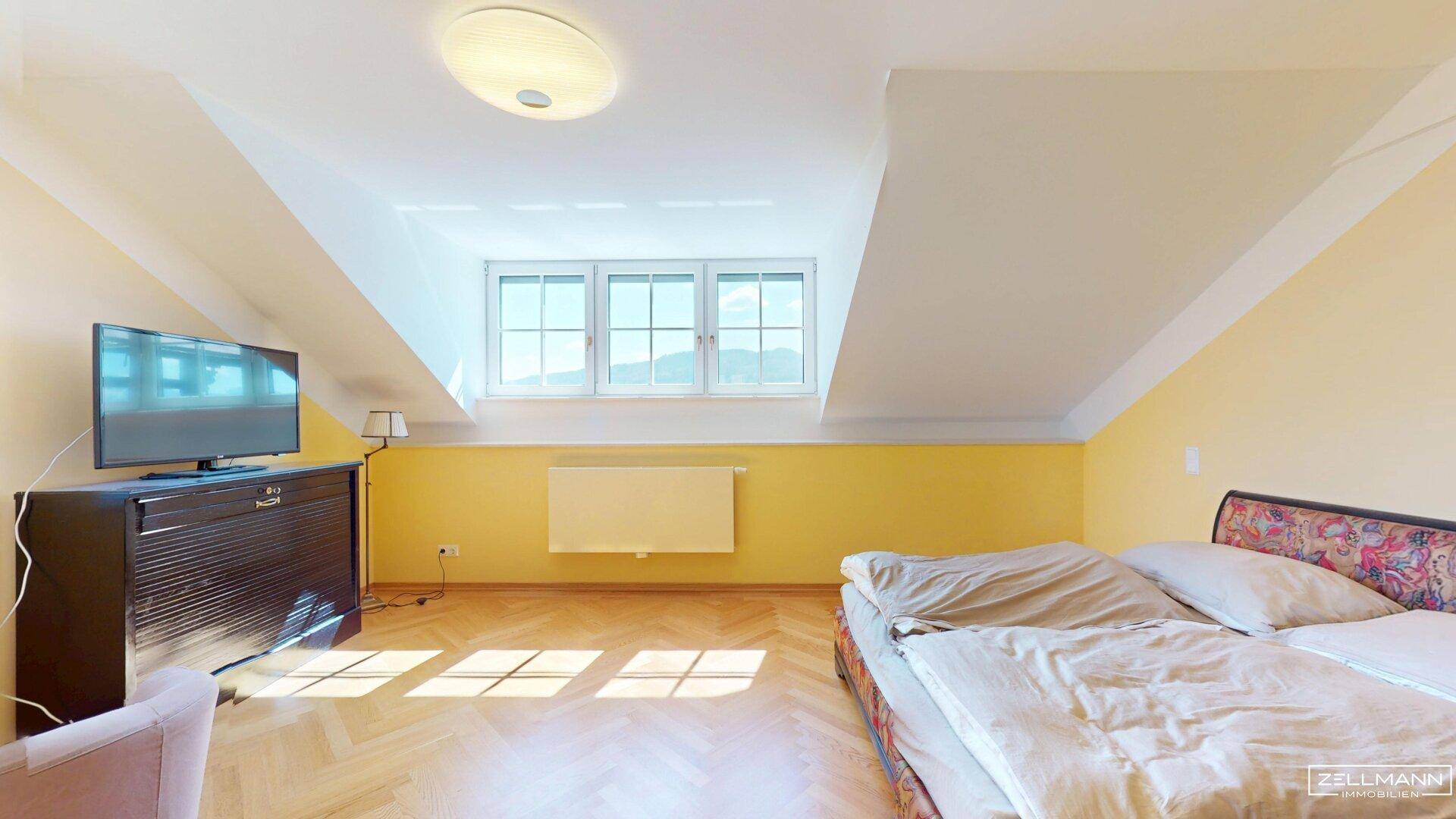 Helles Schlafzimmer im Dachgeschoss mit Schrägen, Parkettboden und gelben Wänden.