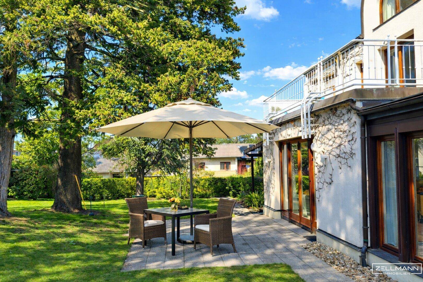 Gemütliche Terrasse mit Gartenmöbeln und Sonnenschirm, umgeben von viel Grün.