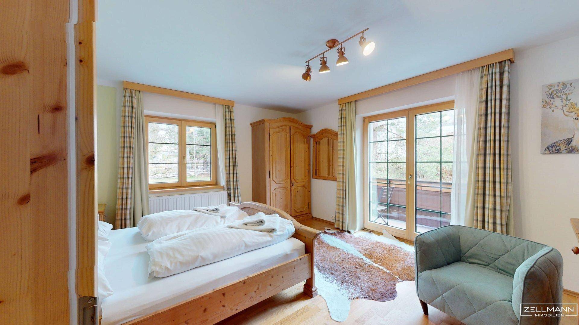Helles Schlafzimmer mit Holzbett, Kleiderschrank und Zugang zu einem Balkon mit Blick ins Grüne.