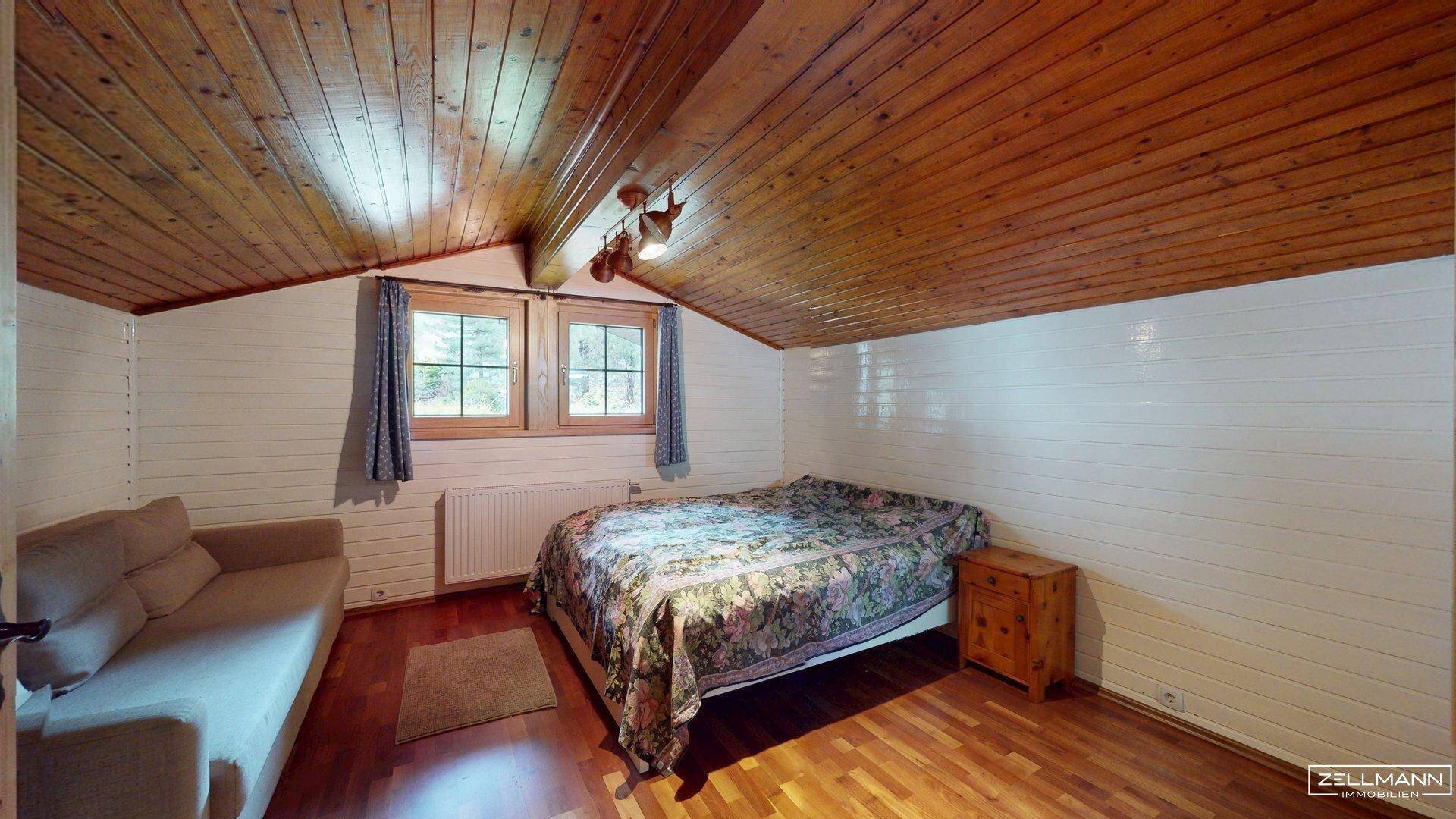 Gemütliches Schlafzimmer im Dachgeschoss mit Holzwänden, Holzboden und schrägen Decken.
