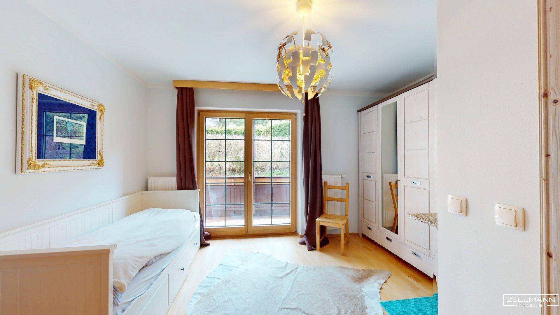 Helles Schlafzimmer mit Einzelbett, Kleiderschrank und Zugang zu einem Balkon.