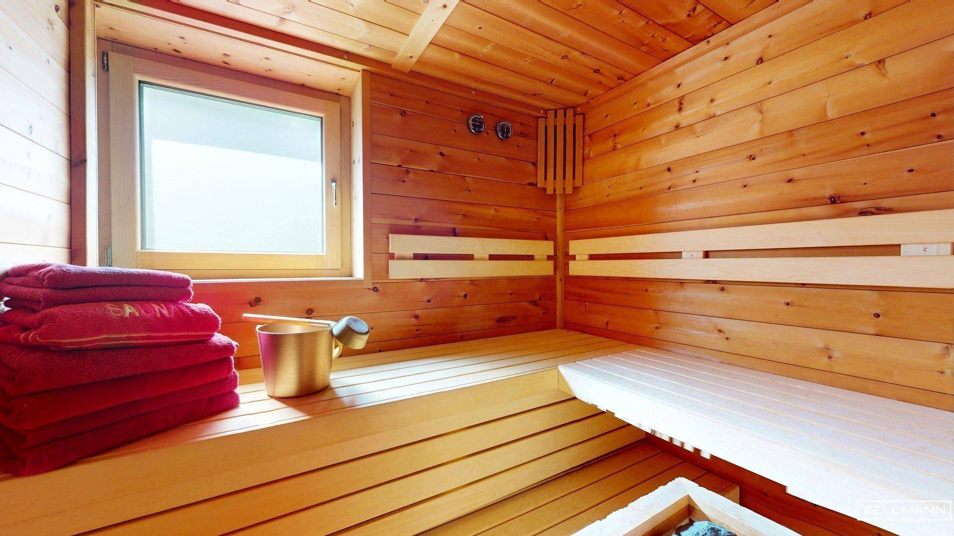 Helle Sauna mit Holzverkleidung, Bänken und einem Fenster für natürliche Belichtung.