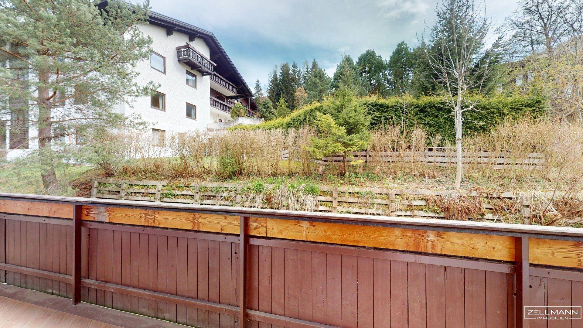 Balkon mit Holzbalkonbrüstung und Blick auf das Gebäude und die grüne Umgebung.