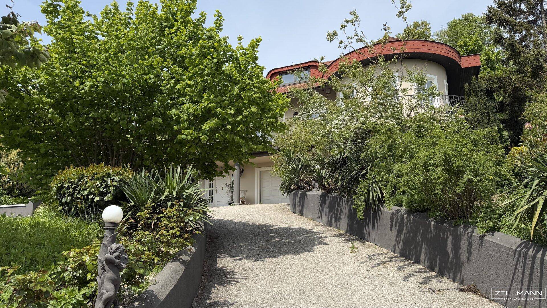 Zufahrt zum Haus mit Garage, umgeben von üppiger Vegetation und Bäumen.