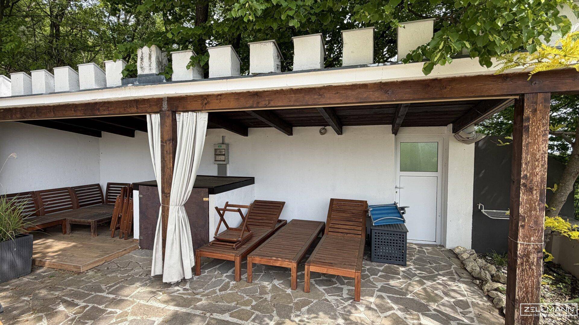 Überdachte Terrasse mit Steinboden, Liegestühlen und einer Holzbank für entspannte Stunden im Freien.