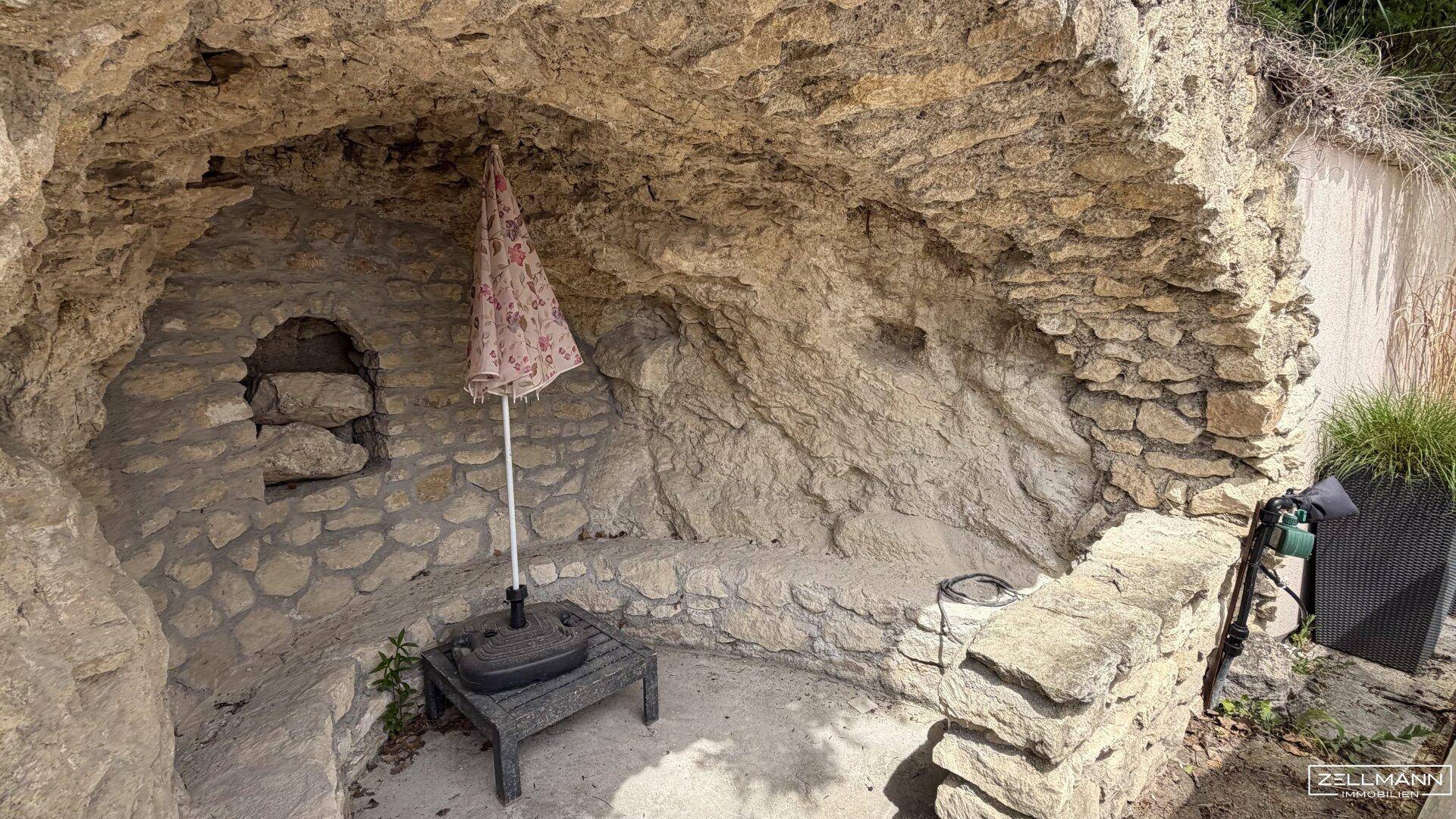 Einzigartiger Felsengarten mit einer natürlichen Grotte und einem Sonnenschirm, ideal für kühle Rückzugsorte.