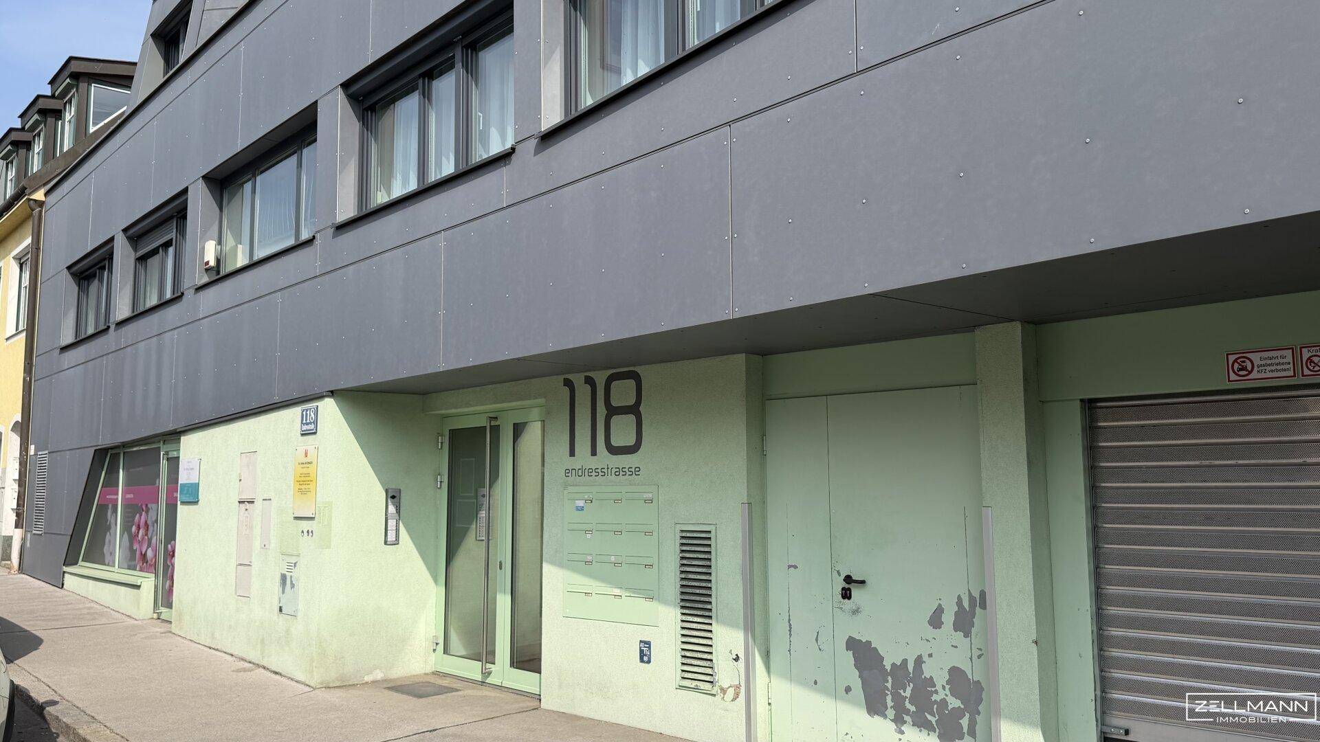 Moderne Gebäudefassade mit Eingangsbereich und Hausnummer an einer belebten Straße.
