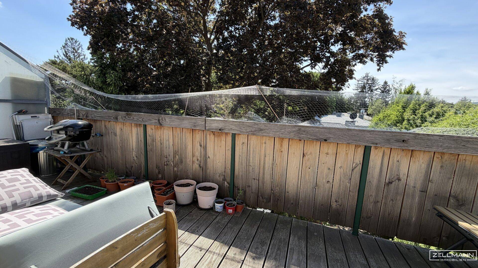 Geräumiger Balkon mit Holzboden, Grill und Blick ins Grüne, ideal für entspannte Stunden.