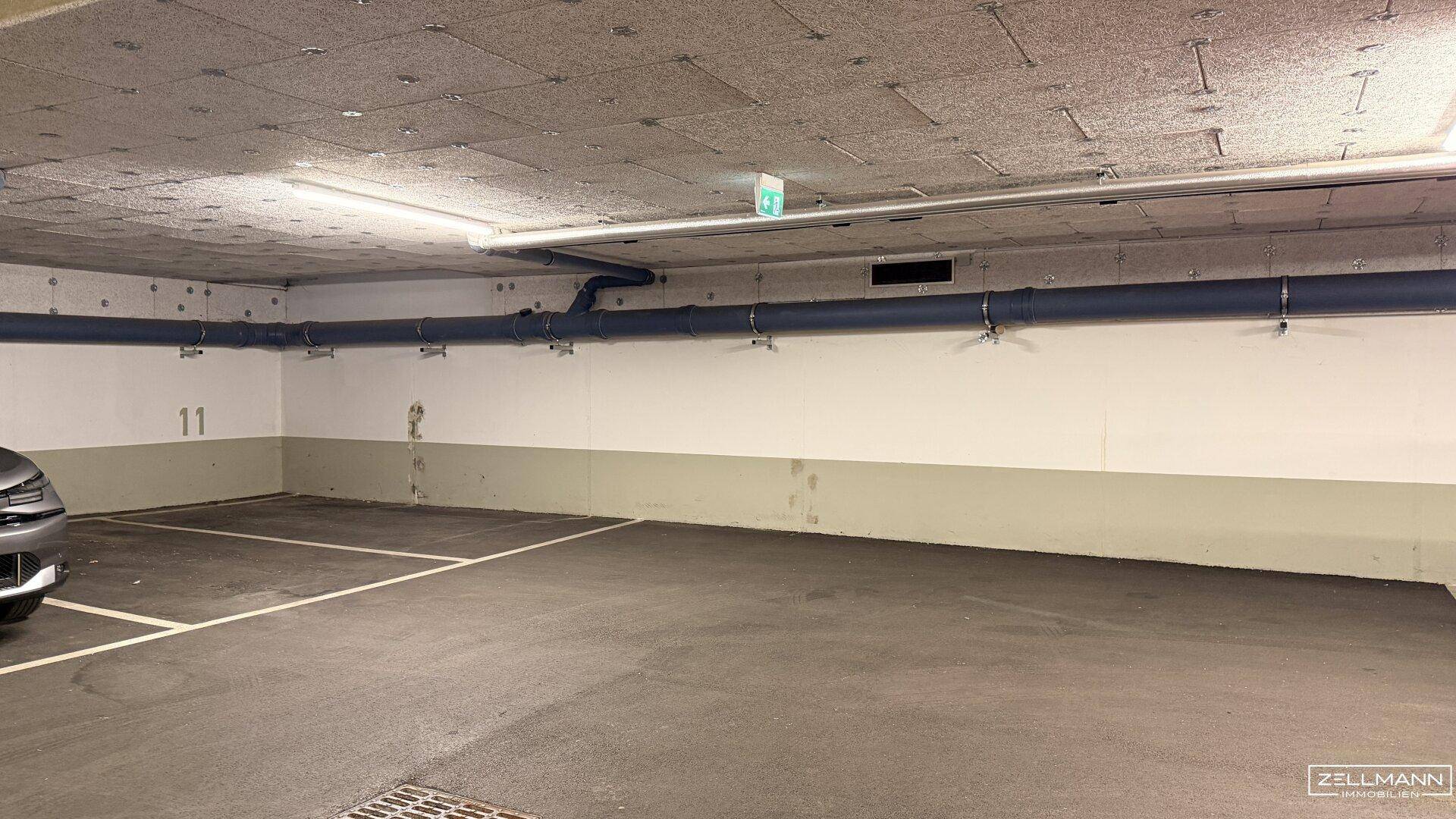 Leerer Tiefgaragenstellplatz Nummer 11 mit sichtbaren Versorgungsleitungen an der Decke.