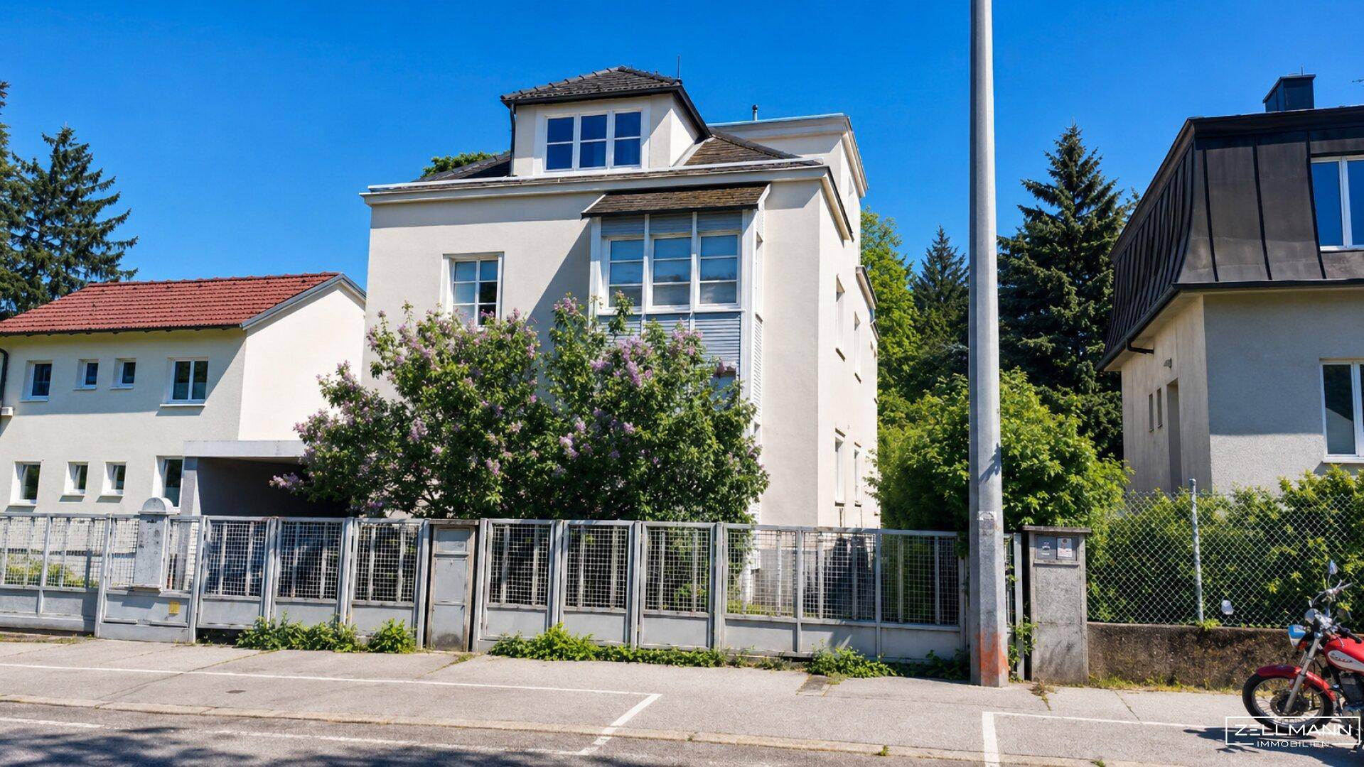 Außenansicht eines Mehrfamilienhauses mit heller Fassade und grüner Bepflanzung an einem sonnigen Tag.