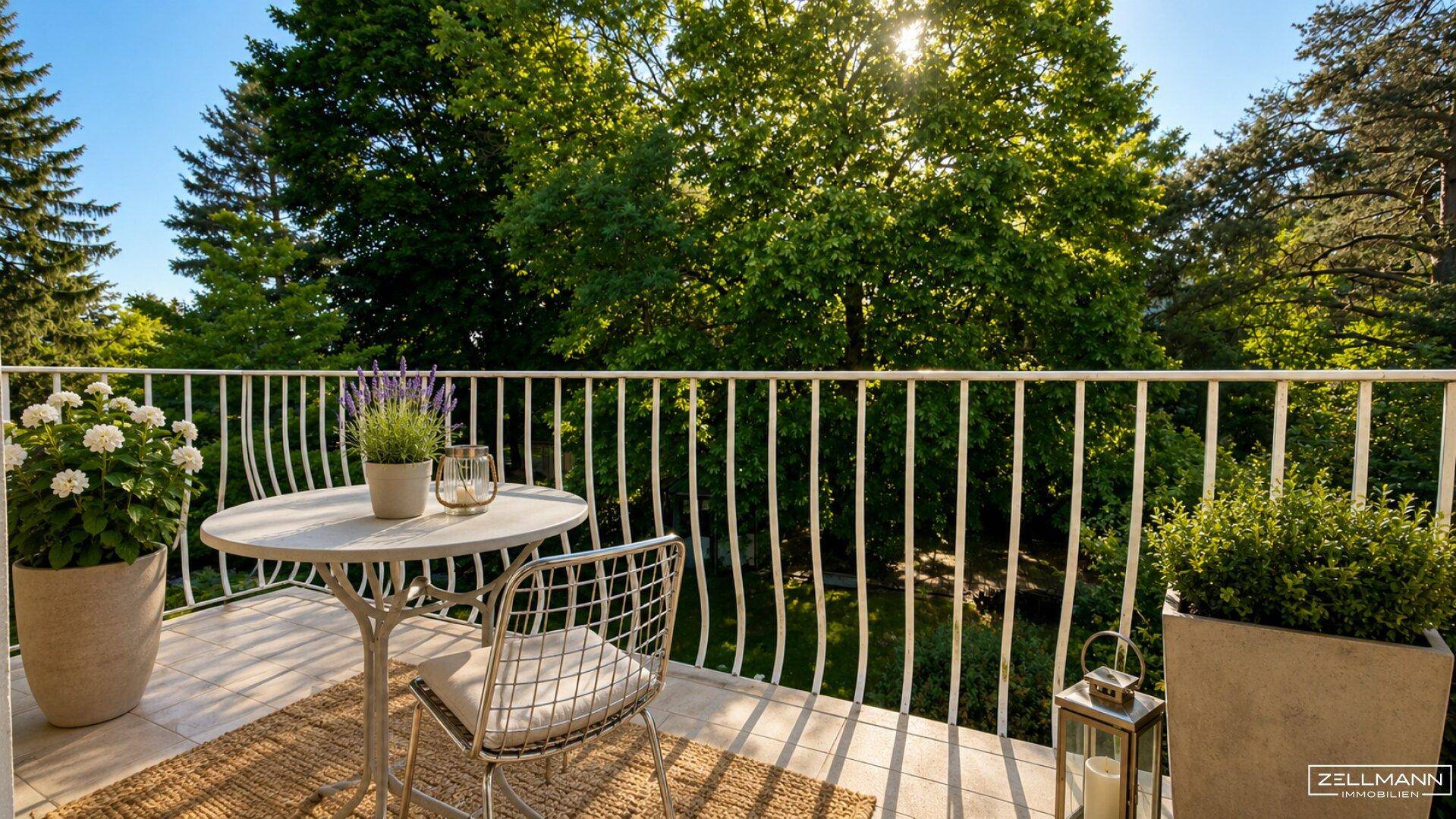 Sonniger Balkon mit kleinem Tisch, Stühlen und üppigem Grünblick auf alte Bäume.