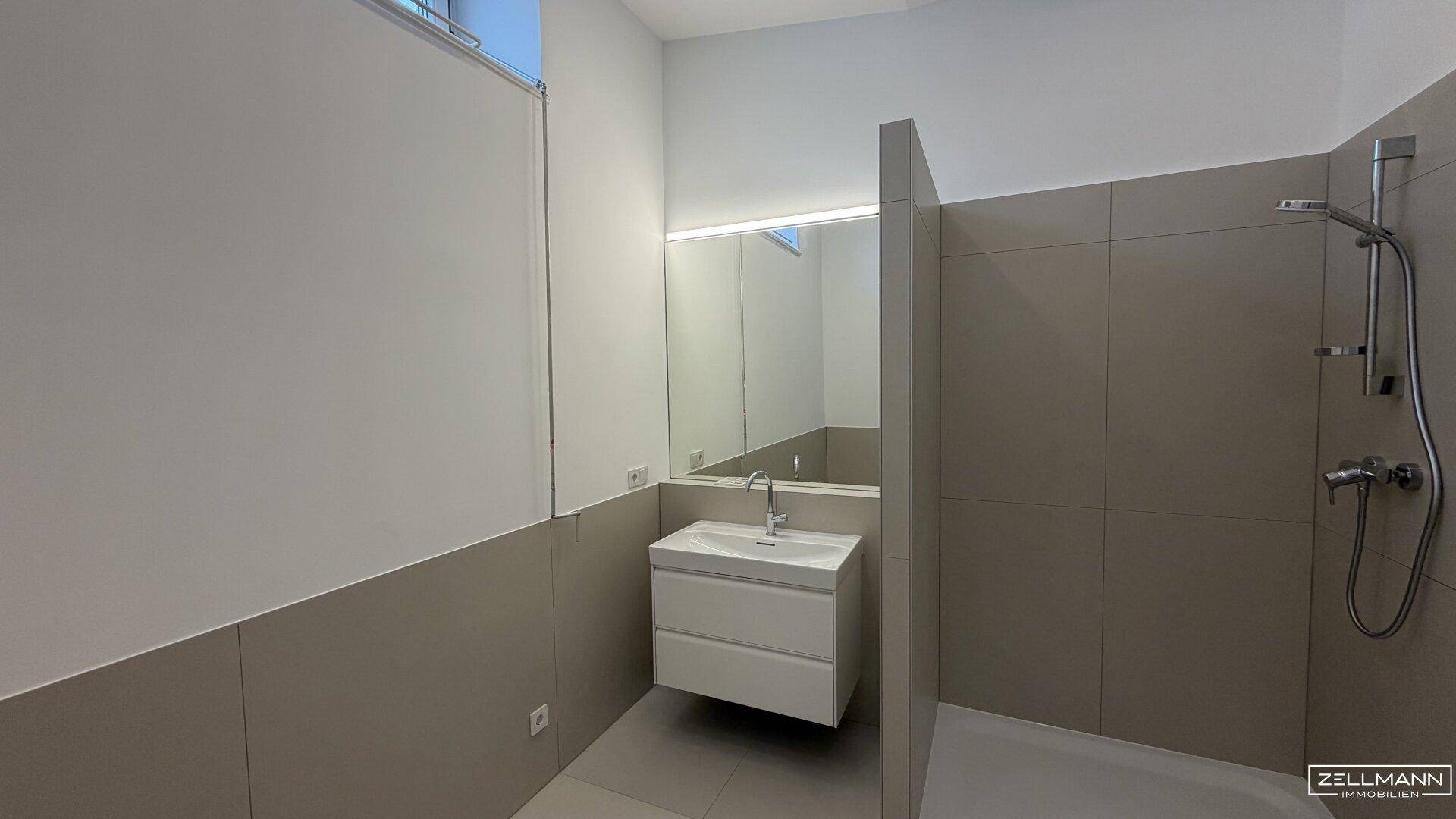 Helles Badezimmer mit modernem Waschtisch, Duschbereich und schmalem Fensterband.