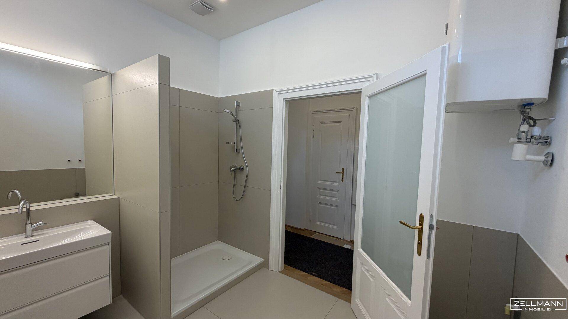 Modernes Badezimmer mit Duschkabine, Waschtisch und Boiler, hell gefliest.