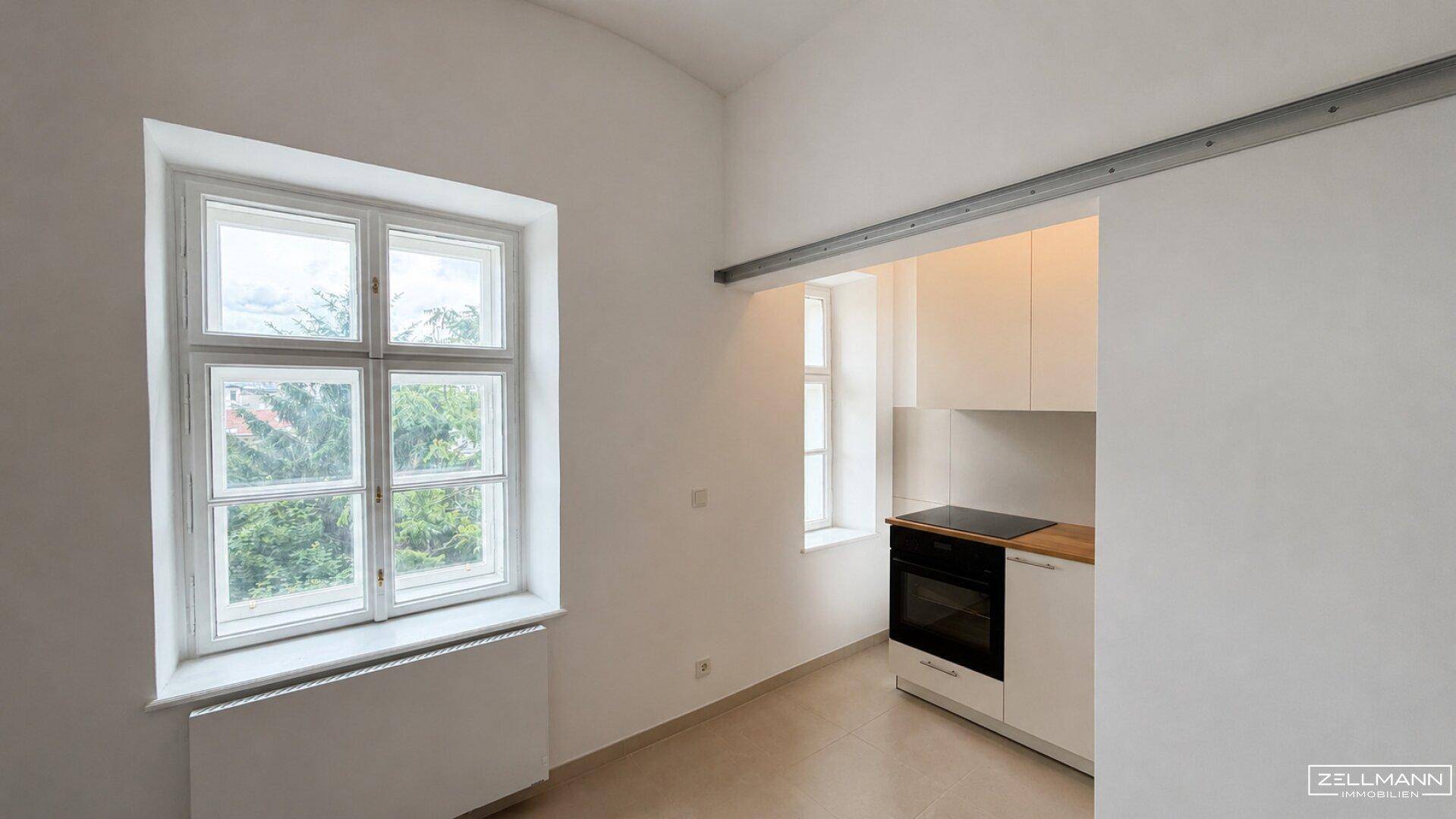 Kompakte Küchenzeile mit Fenster und Holzarbeitsplatte, integriert in einen hellen Raum.