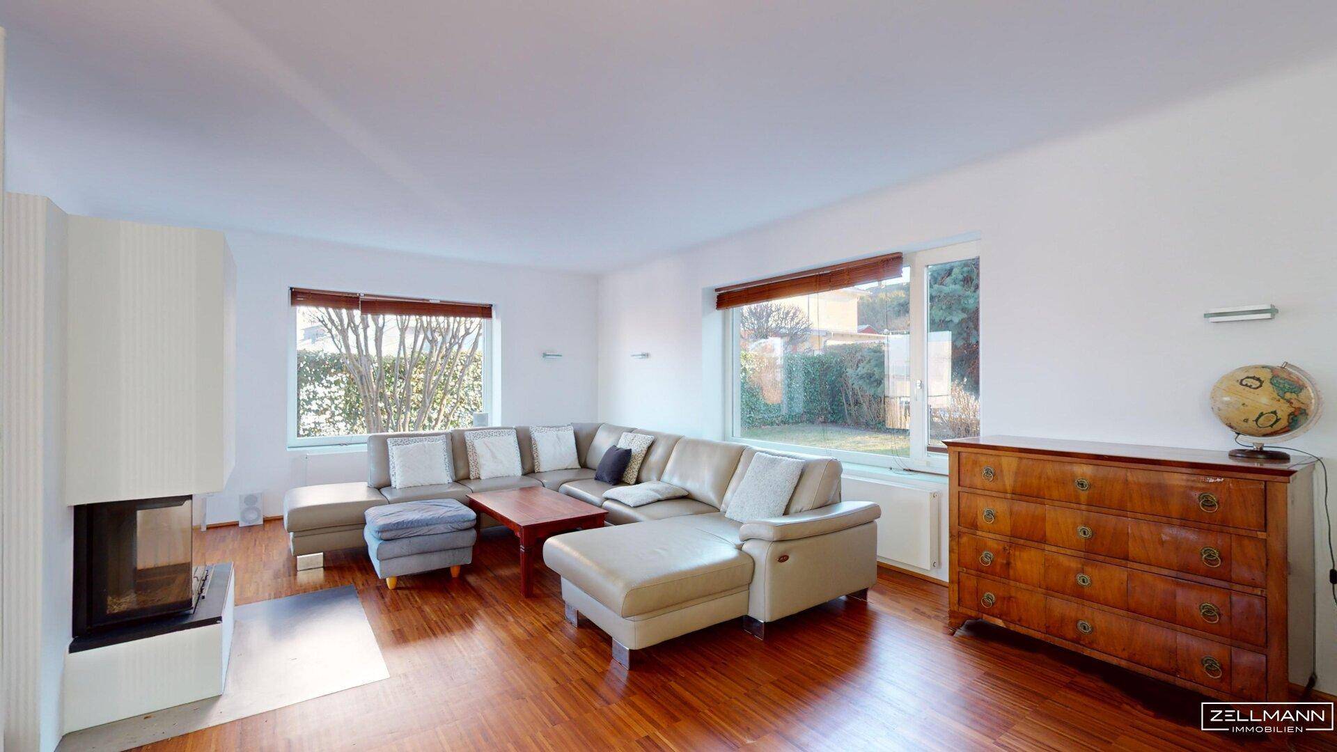 Gemütliches Wohnzimmer mit großem Ecksofa, Kamin und Blick in den Garten.