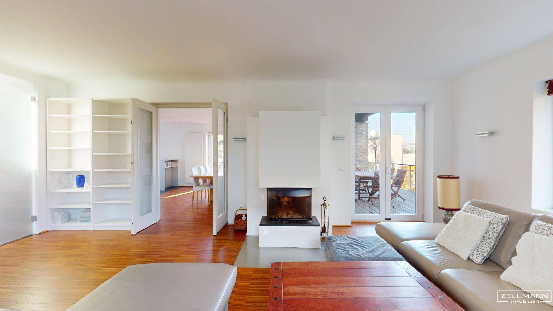 Helles Wohnzimmer mit Kamin, Parkettboden und Zugang zu einer Außenterrasse.