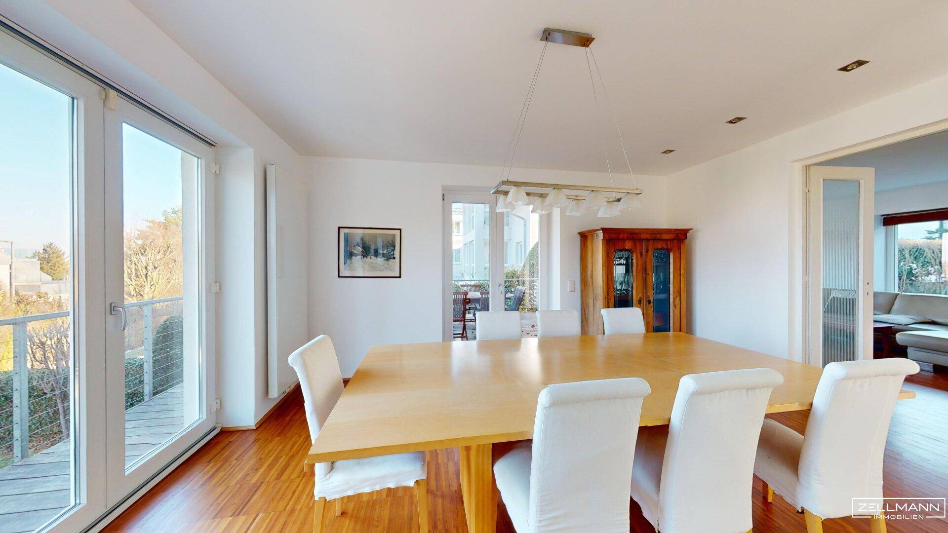 Eleganter Essbereich mit großem Holztisch und Stühlen, bietet Zugang zum Balkon.
