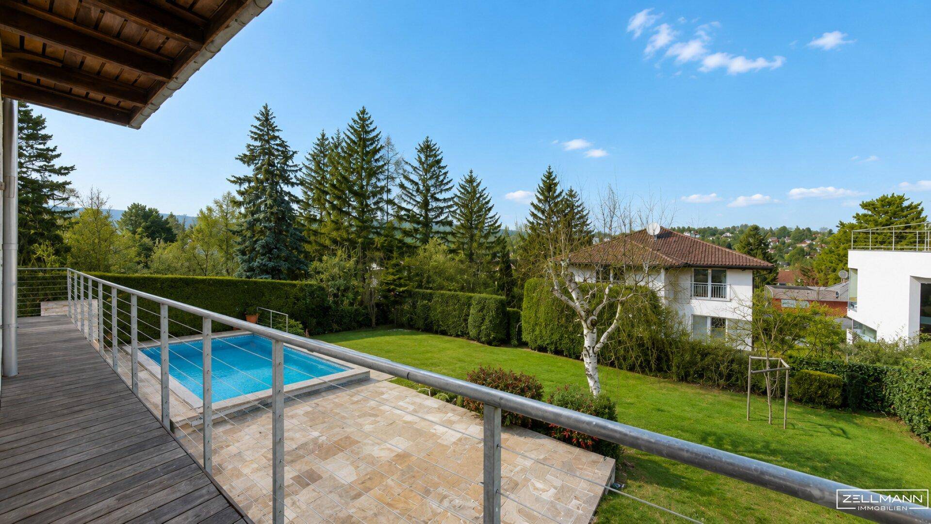 Weitläufiger Garten mit Pool und Holzterrasse, umgeben von hohen Bäumen und Hecken.