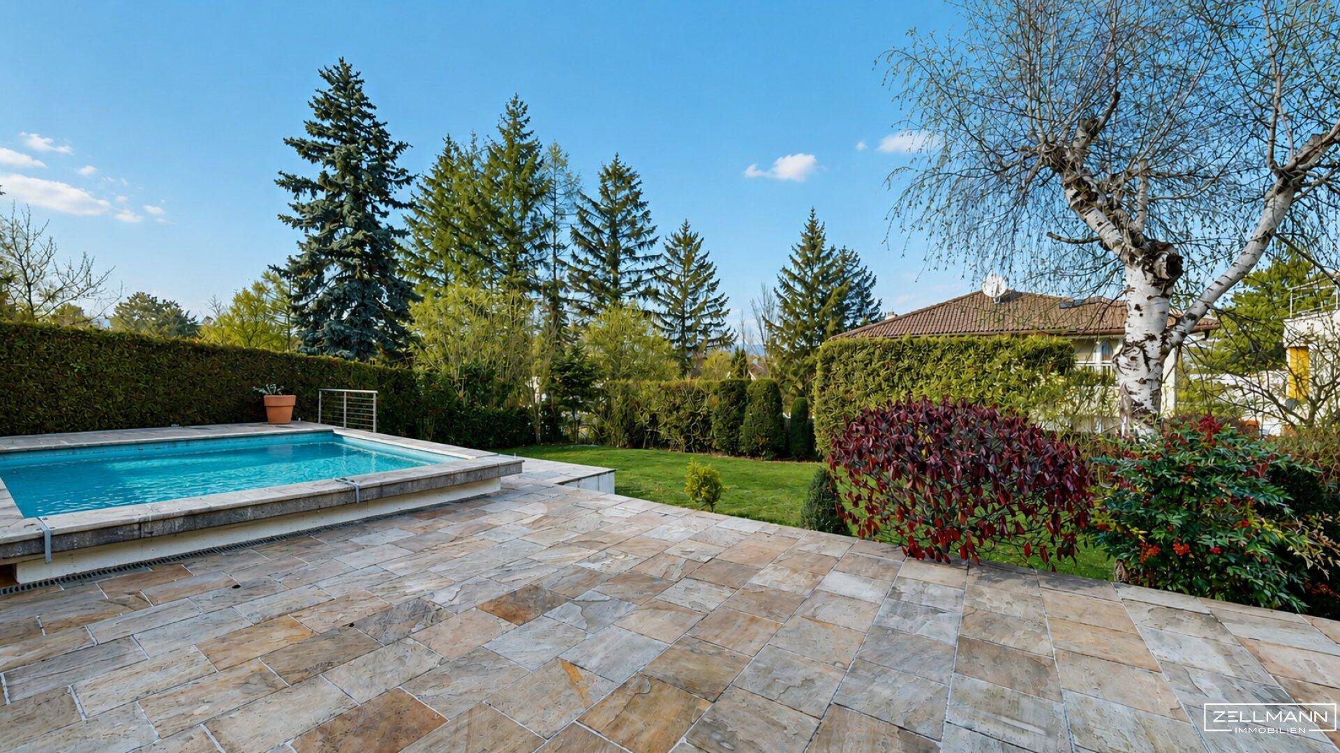 Sonniger Poolbereich mit Steinfliesen und gepflegtem Garten, ideal zum Entspannen im Freien.