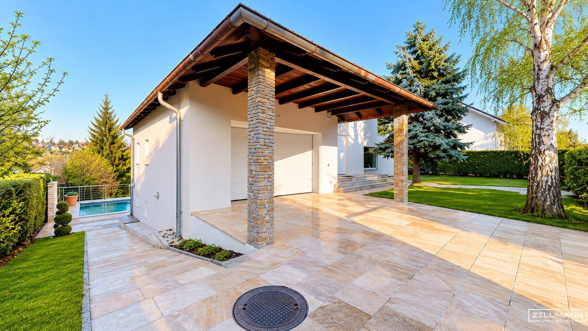 Seitlicher Blick auf das Haus mit Garage, gepflasterter Auffahrt und Zugang zum Poolbereich.