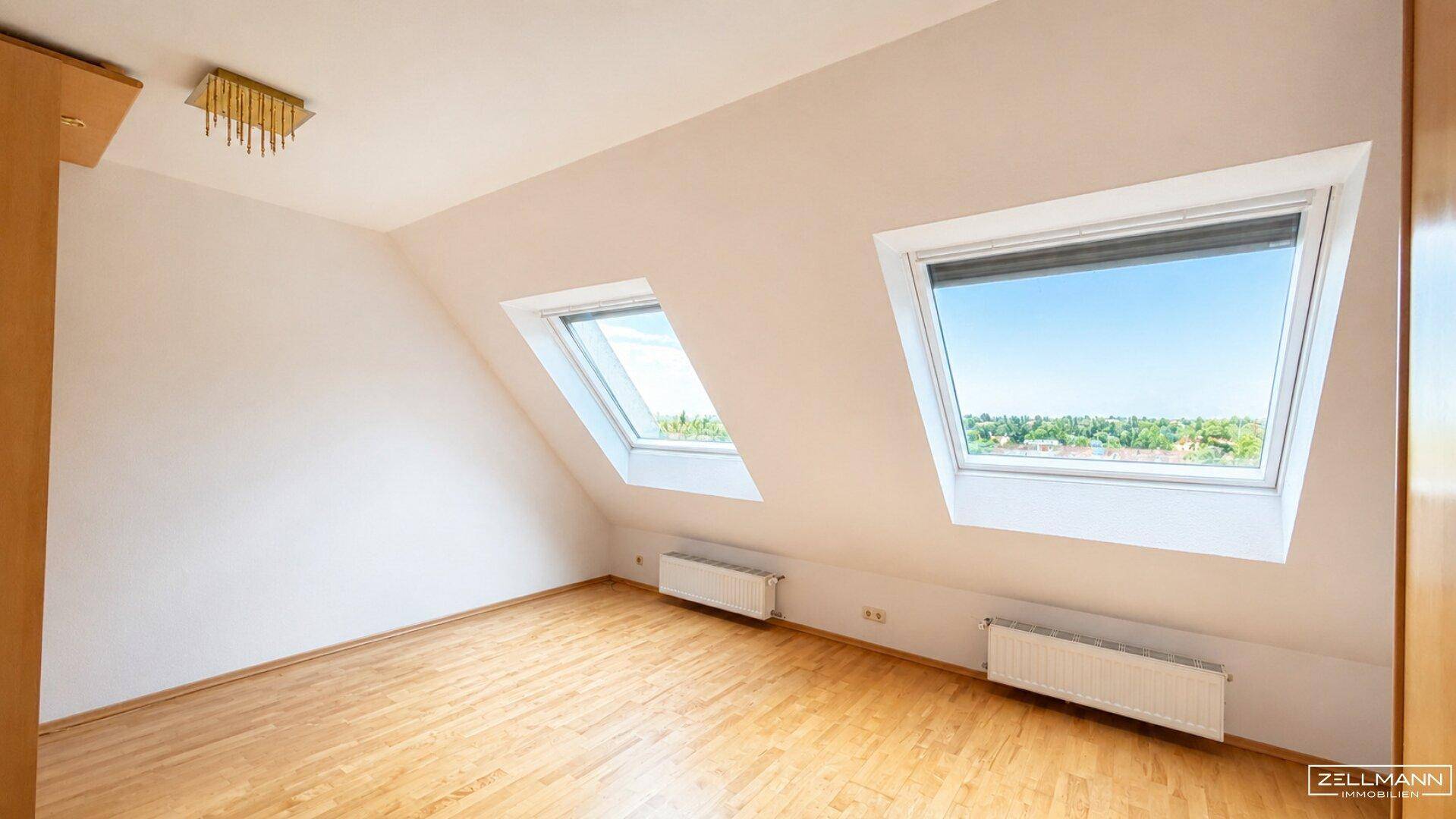 Geräumiges Dachzimmer mit zwei großen Dachfenstern und Holzboden.