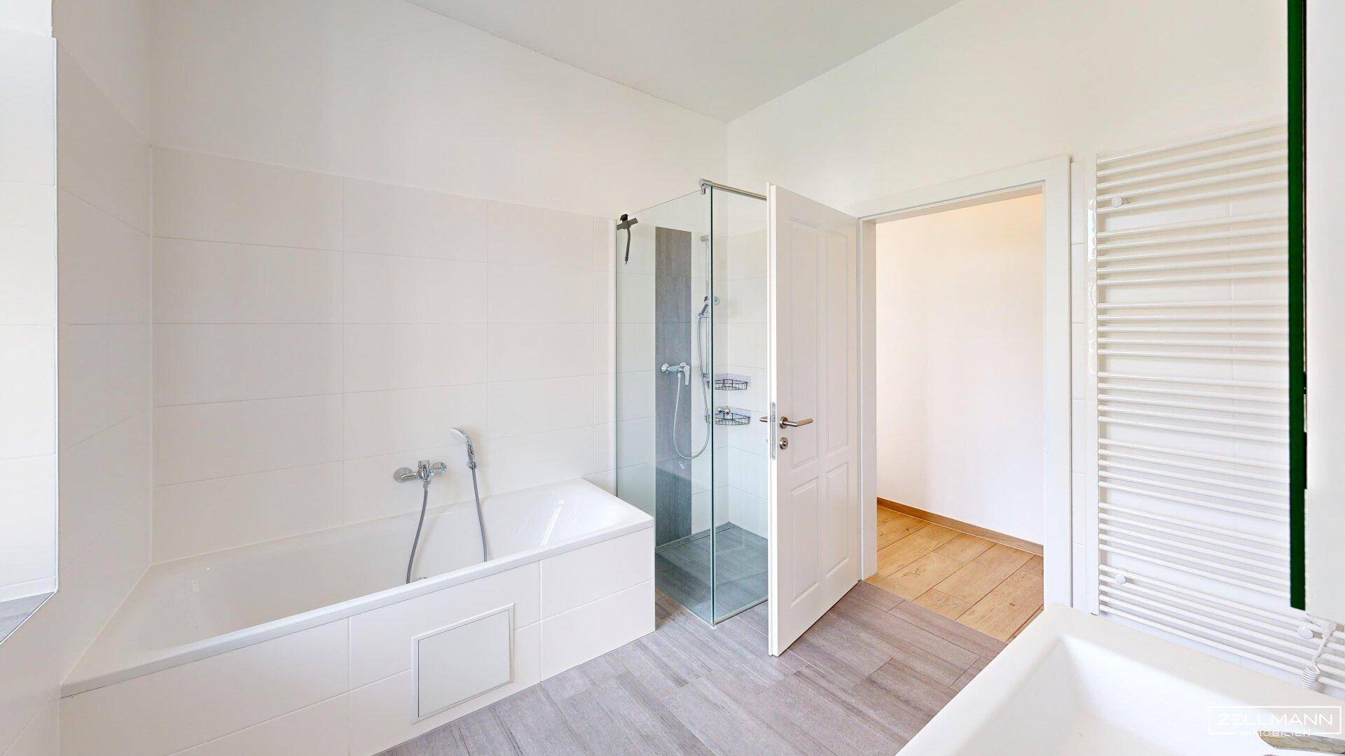 Helles Badezimmer mit Badewanne, Duschkabine und beheiztem Handtuchhalter.