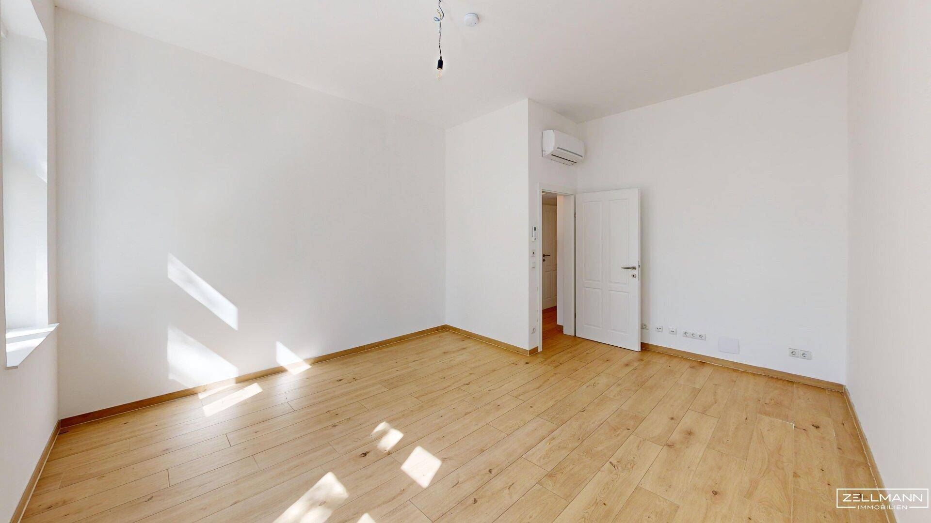 Helles Schlafzimmer mit Holzboden, weiß gestrichenen Wänden und Klimaanlage.