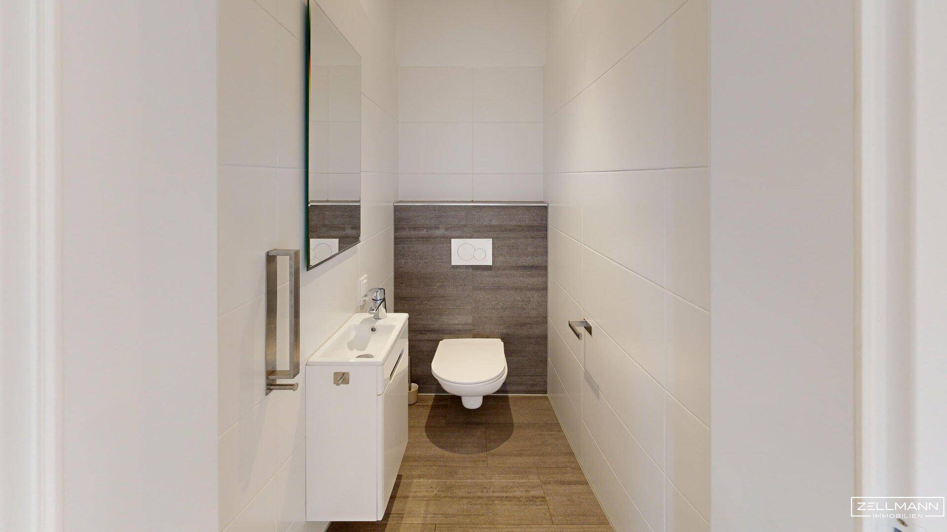 Modernes Gäste-WC mit wandhängender Toilette, kleinem Waschbecken und Spiegel.