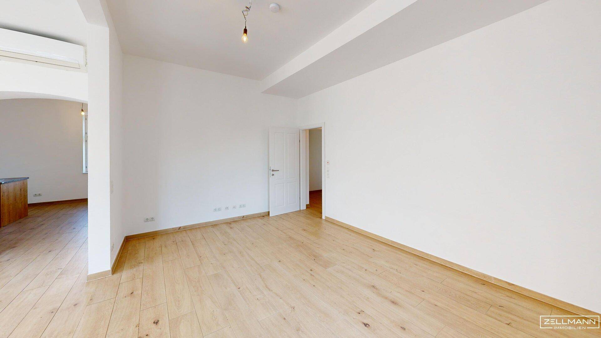 Geräumiges Zimmer mit hellem Holzboden und weiß gestrichenen Wänden, ideal als Wohnbereich.