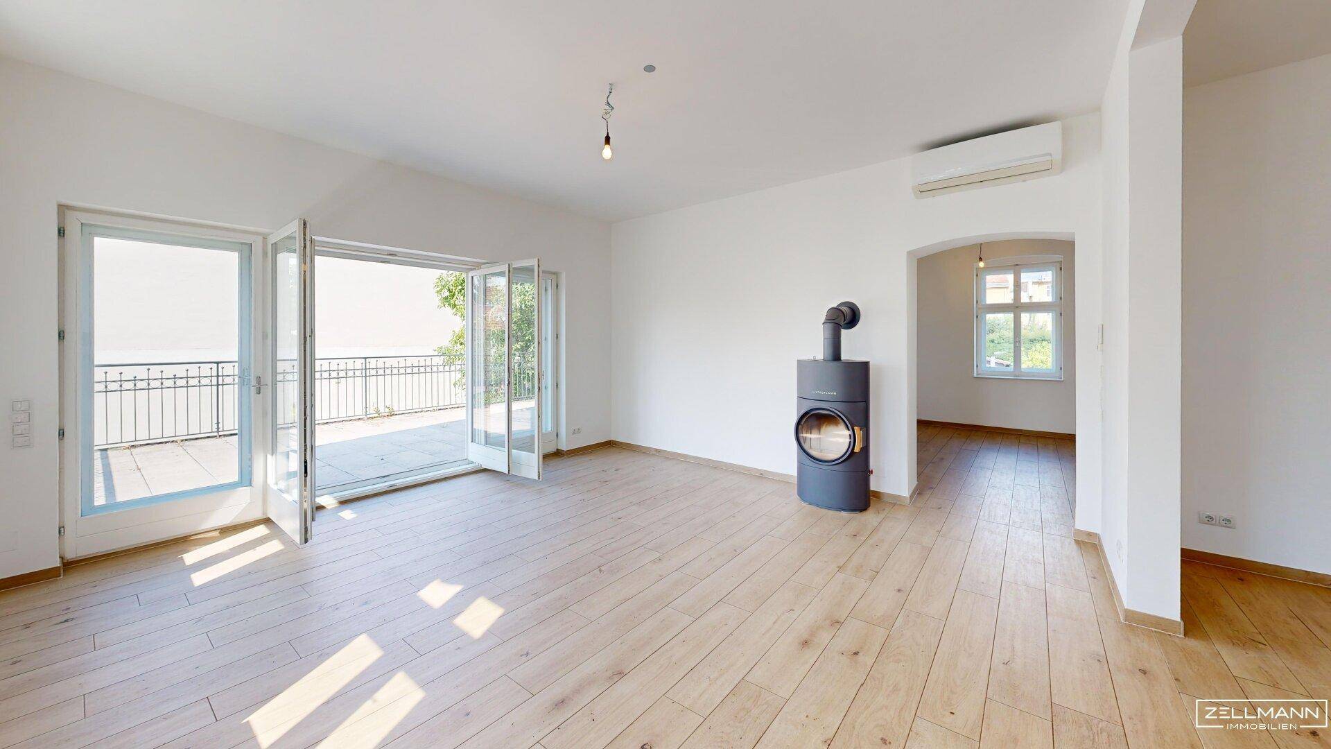 Helles Wohnzimmer mit Holzboden, modernem Kaminofen und Zugang zur großen Terrasse.