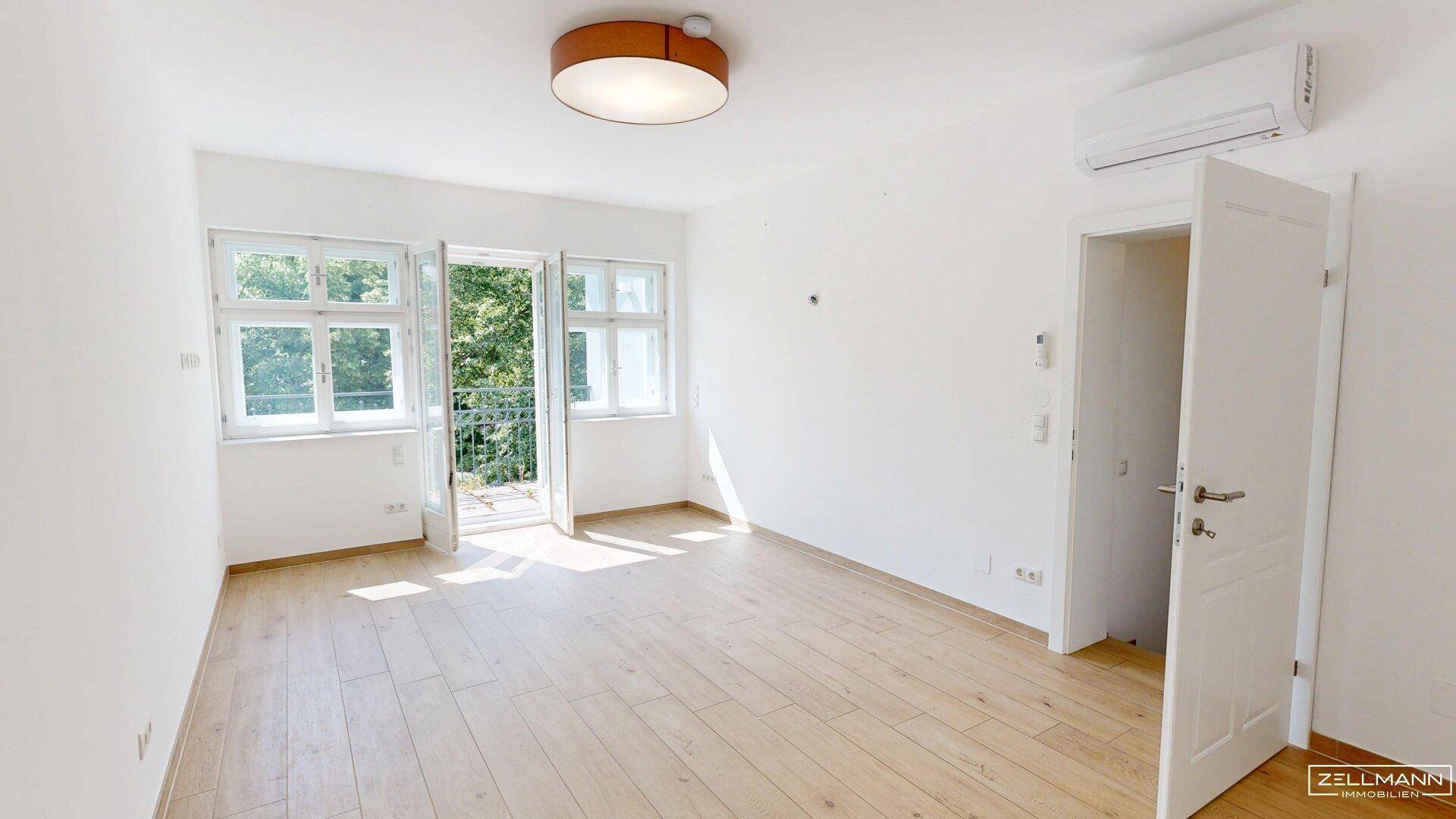 Helles Schlafzimmer mit Holzboden, Klimaanlage und Zugang zu einem kleinen Balkon.