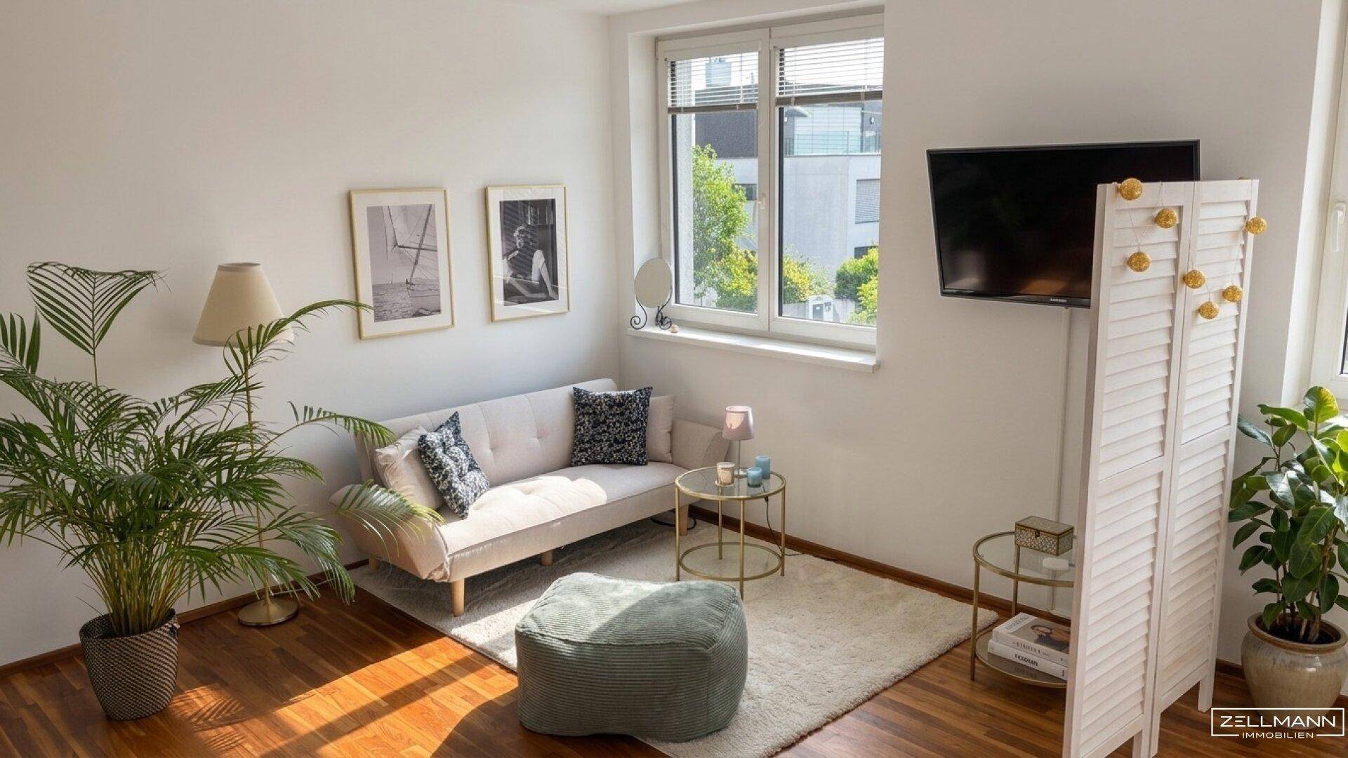 Gemütliches Wohnzimmer mit Sofa, Holzboden und großen Fenstern für viel Tageslicht.