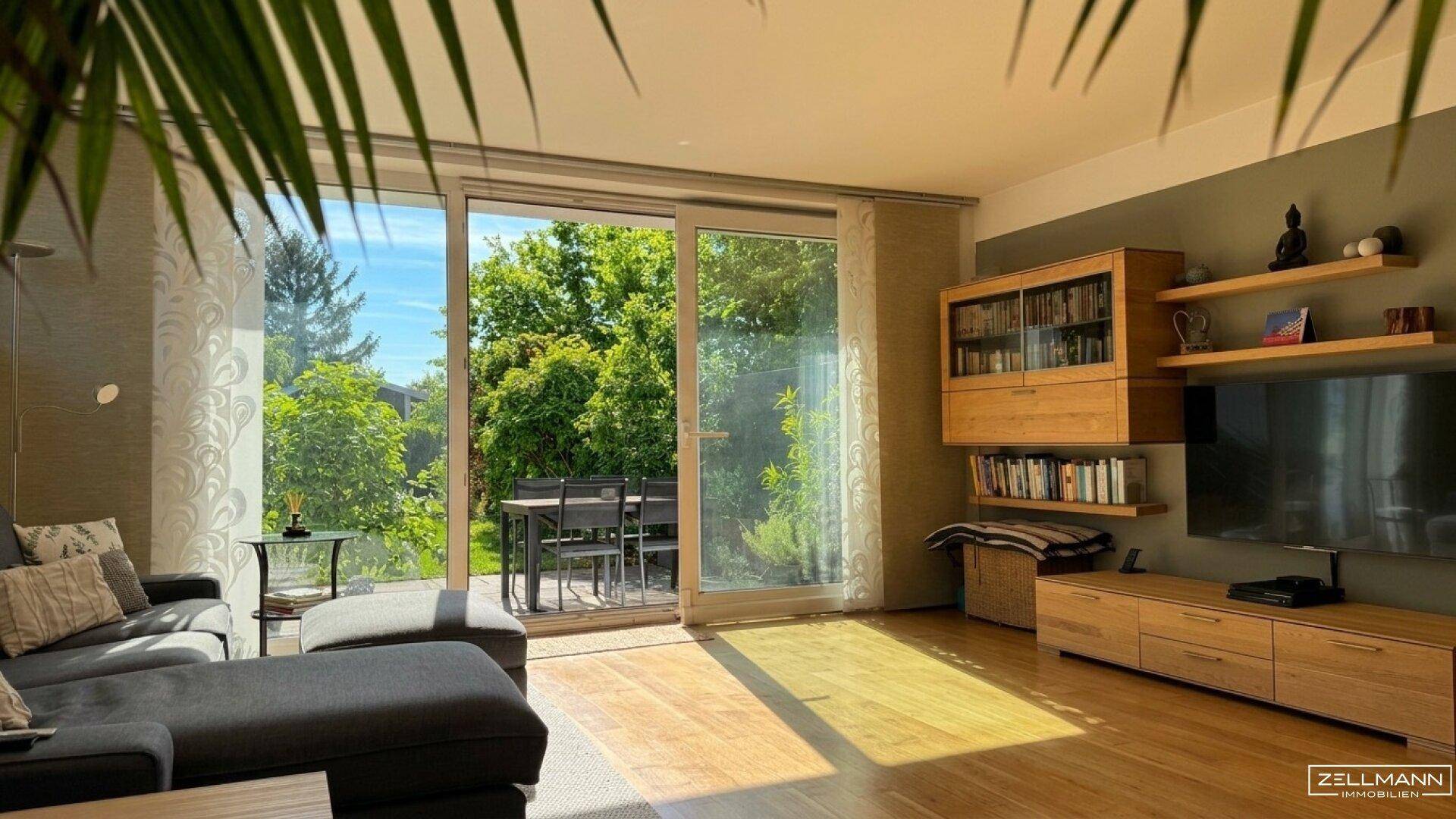 Lichtdurchflutetes Wohnzimmer mit Holzboden, großzügigen Fenstern und Blick ins Grüne.